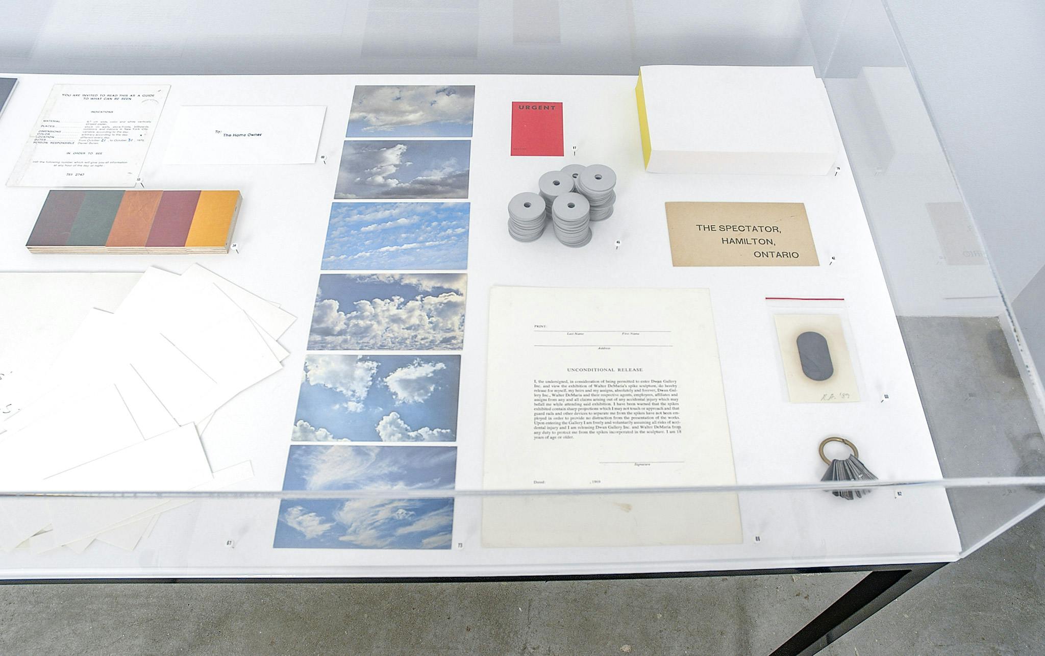 Detail of artworks by Micah Lexier. In a display case, a variety of objects such as postcards and photographs of the blue sky are placed. 