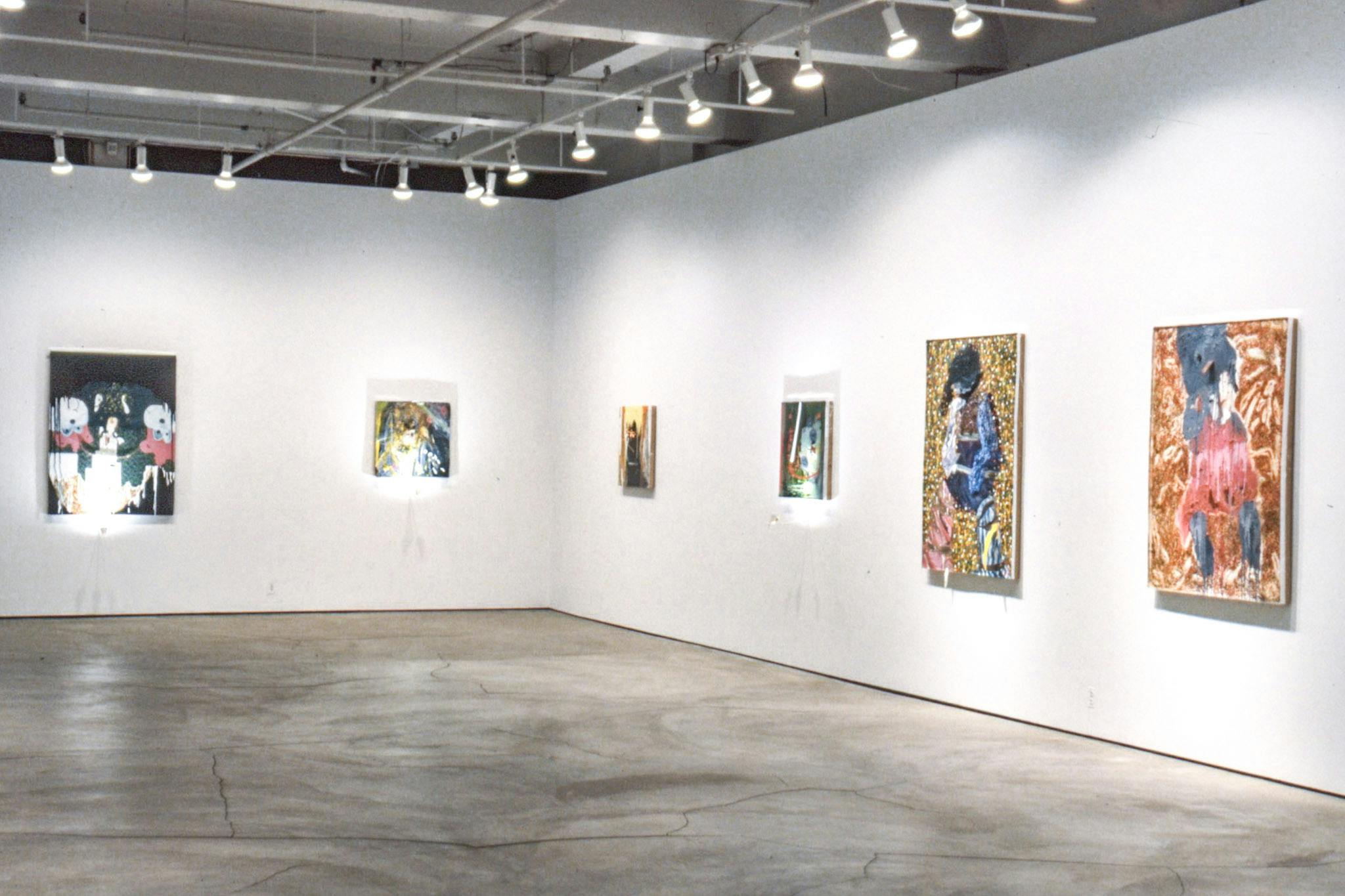 Six visible paintings on the walls in the corner of a gallery. The paintings are colourful and vary in size. Three of them have bright lights attached just underneath them, creating bright spots. 