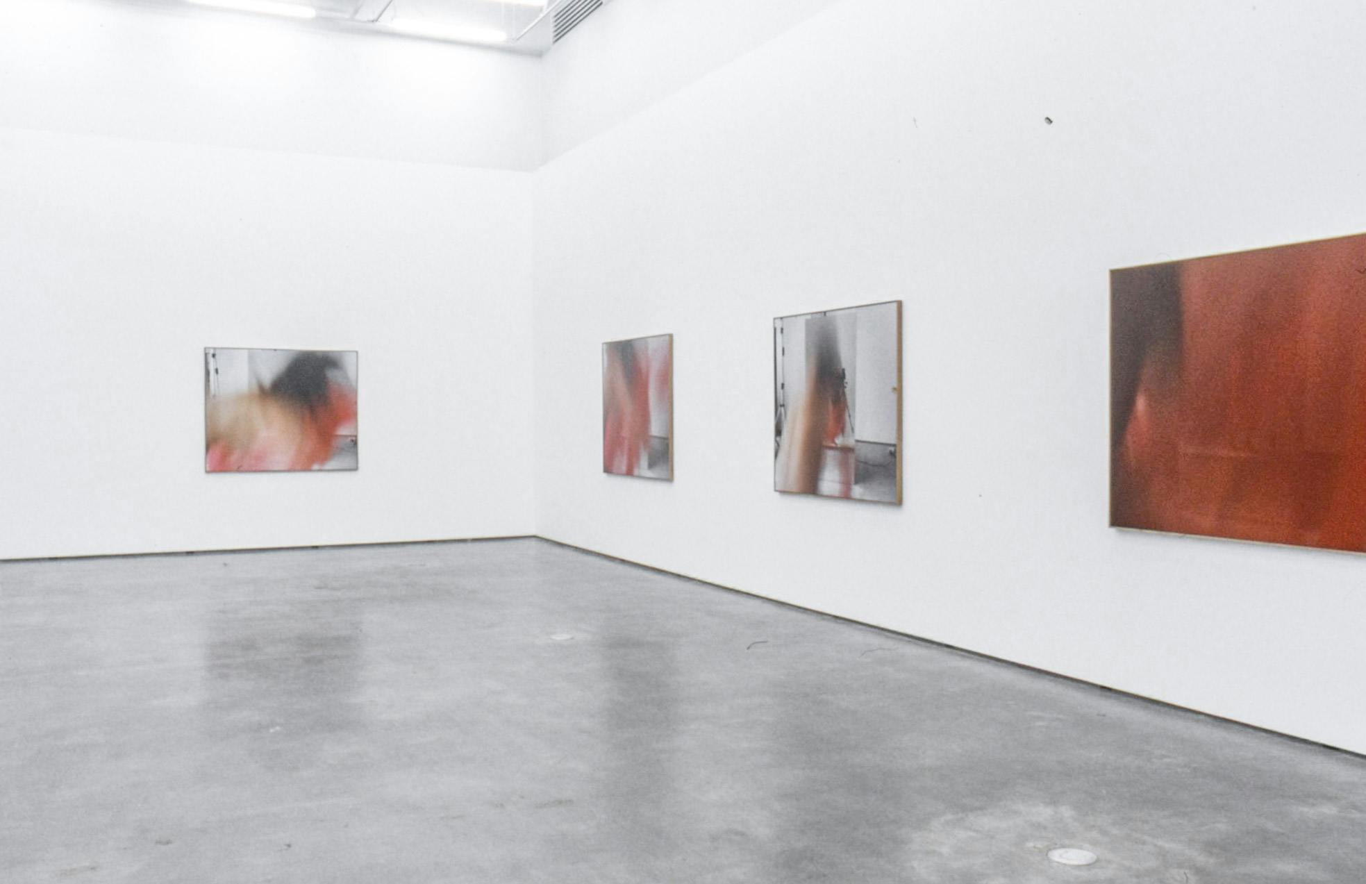 Large-sized photographs are installed on the gallery walls. Four photographs visible in this image all show blurred images of a person dancing with a piece of red-coloured fabric. 
