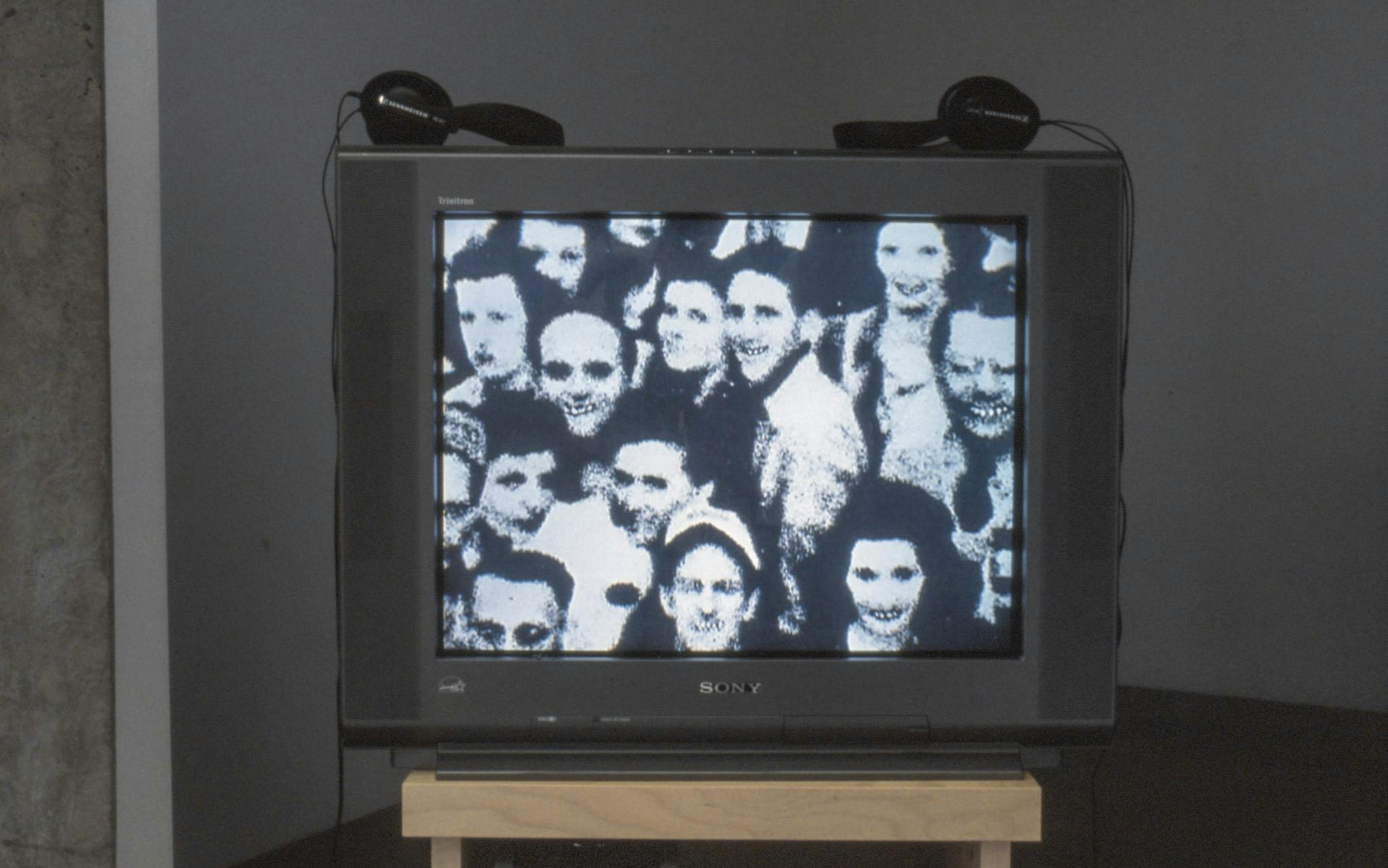 Detail of a video installation by Marina Roy. A CRT TV shows a black and white photographed image of people closely standing with each other and smiling at the camera. 