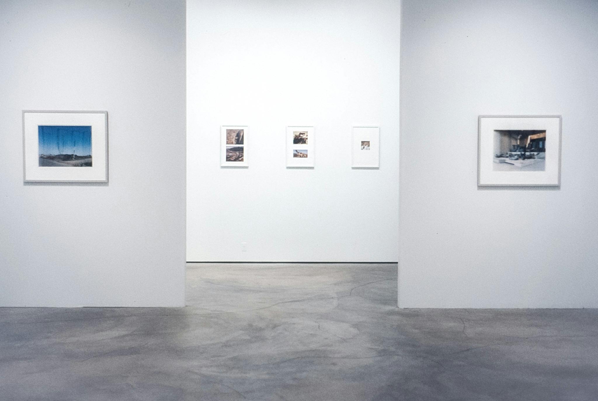 A gallery space with two walls framing a hallway in the background. The walls on the left and the right have a large framed photo work on them. In the centre, the hallway has three framed photo works.