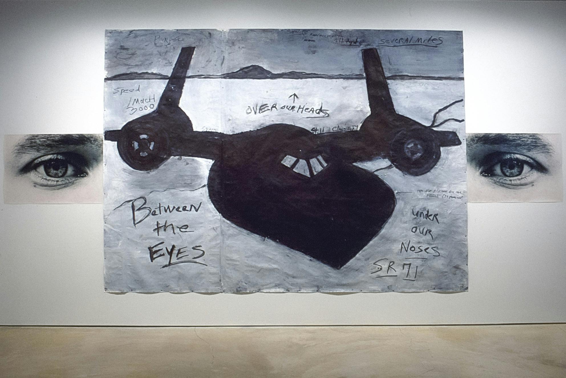 A large black and white drawing is installed on the gallery wall. A black airplane is drawn above the word “SR71." This drawing is placed in between a pair of photographs of human eyes.