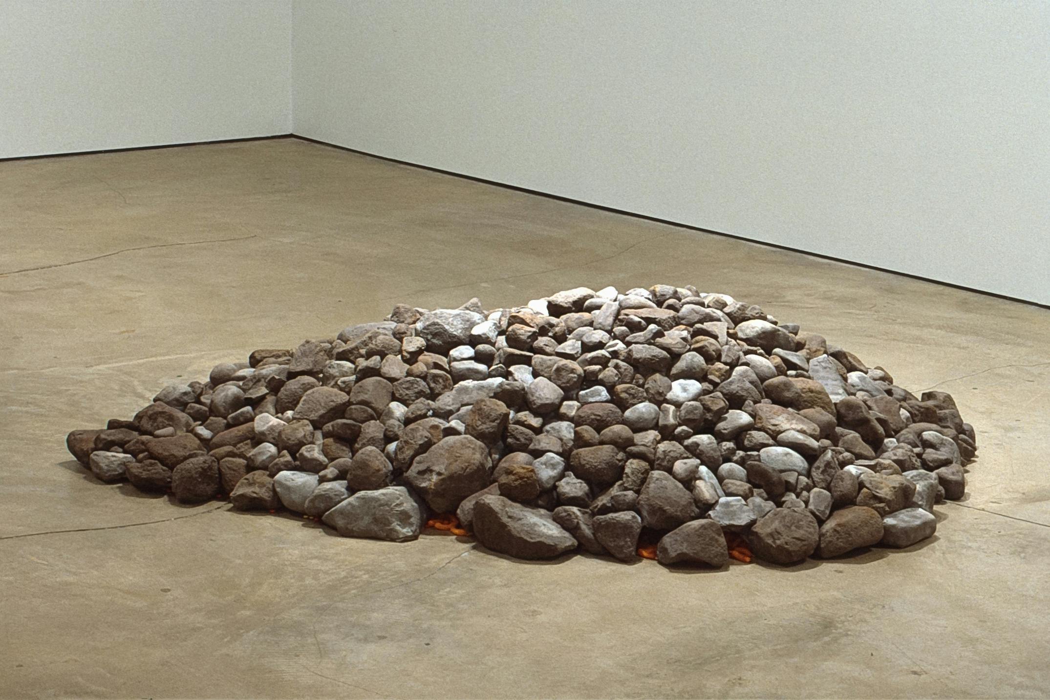 A pile of small rocks and stones is placed on the gallery floor. The pile is quite low. A layer of orange strings, which seems to be either ropes or fried snacks, are visible under the rocks. 