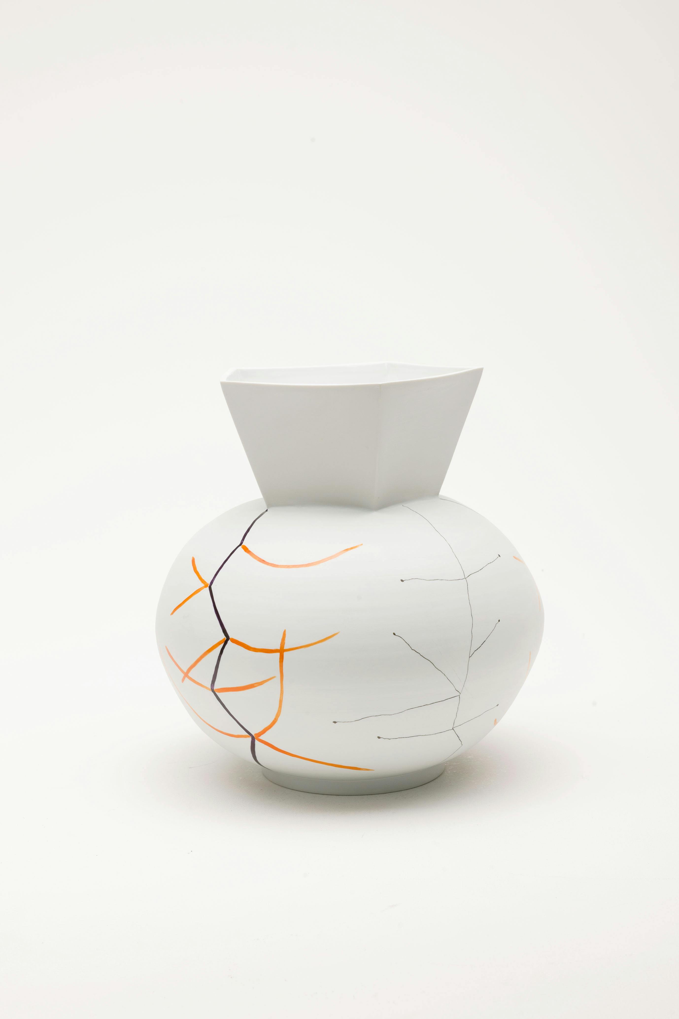  A white ceramic vase painted with then orange, black and grey lines. The vase has a bulbous bottom and geometric neck. 