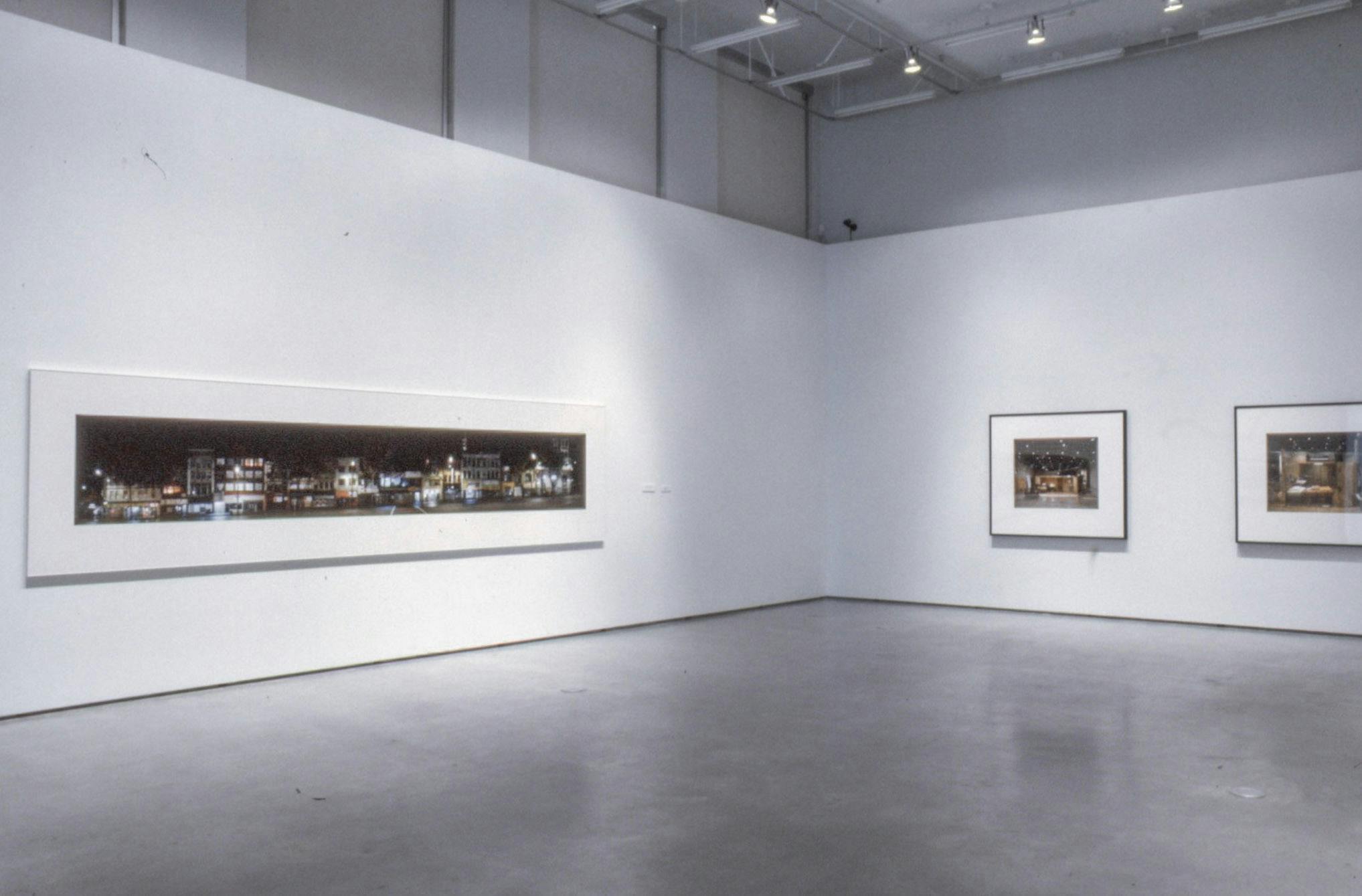 Several photographs are mounted on the gallery walls. The one mounted on the left-hand side wall is a panorama view of a street taken at night. Two smaller photographs are mounted on the other wall.