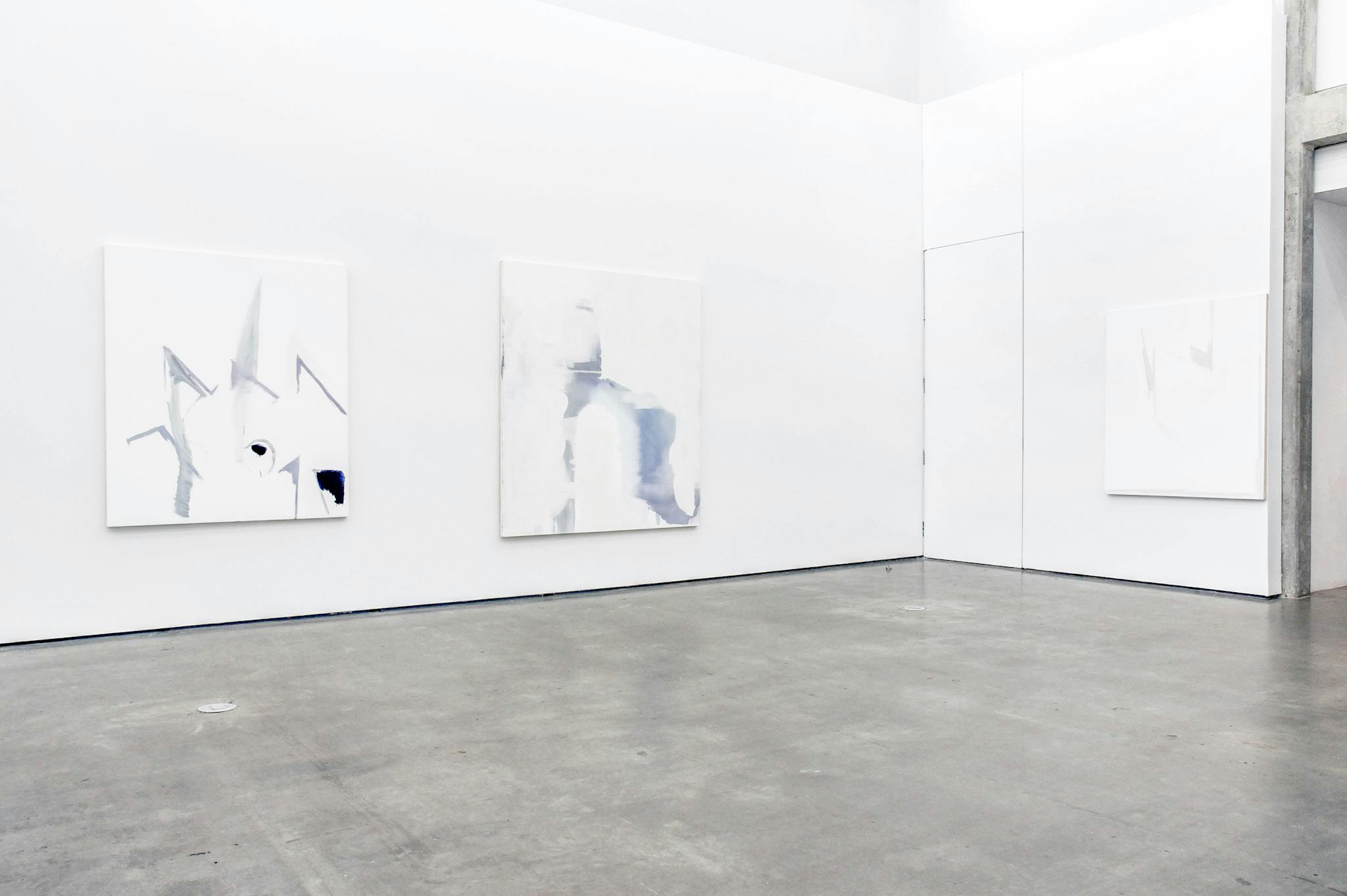 Three large abstract paintings are installed on the gallery walls. Overall, they are white paintings on which some strokes of tinted blue and light purple colours are drawn.  