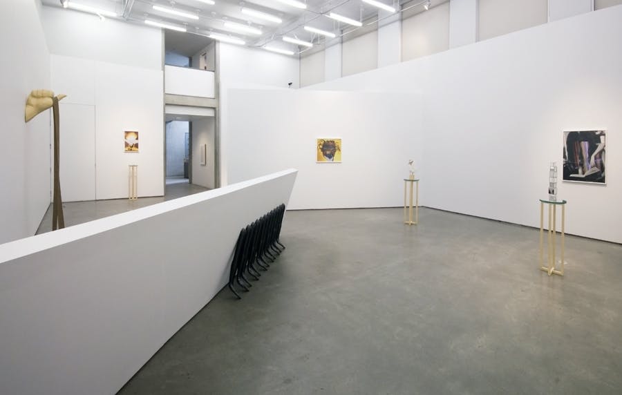 Installation shot of Elizabeth Zvonars work in a gallery. Three images hang on different walls. Small tables with cubes on top sit throughout the space, a large rectangular block sits to the left.