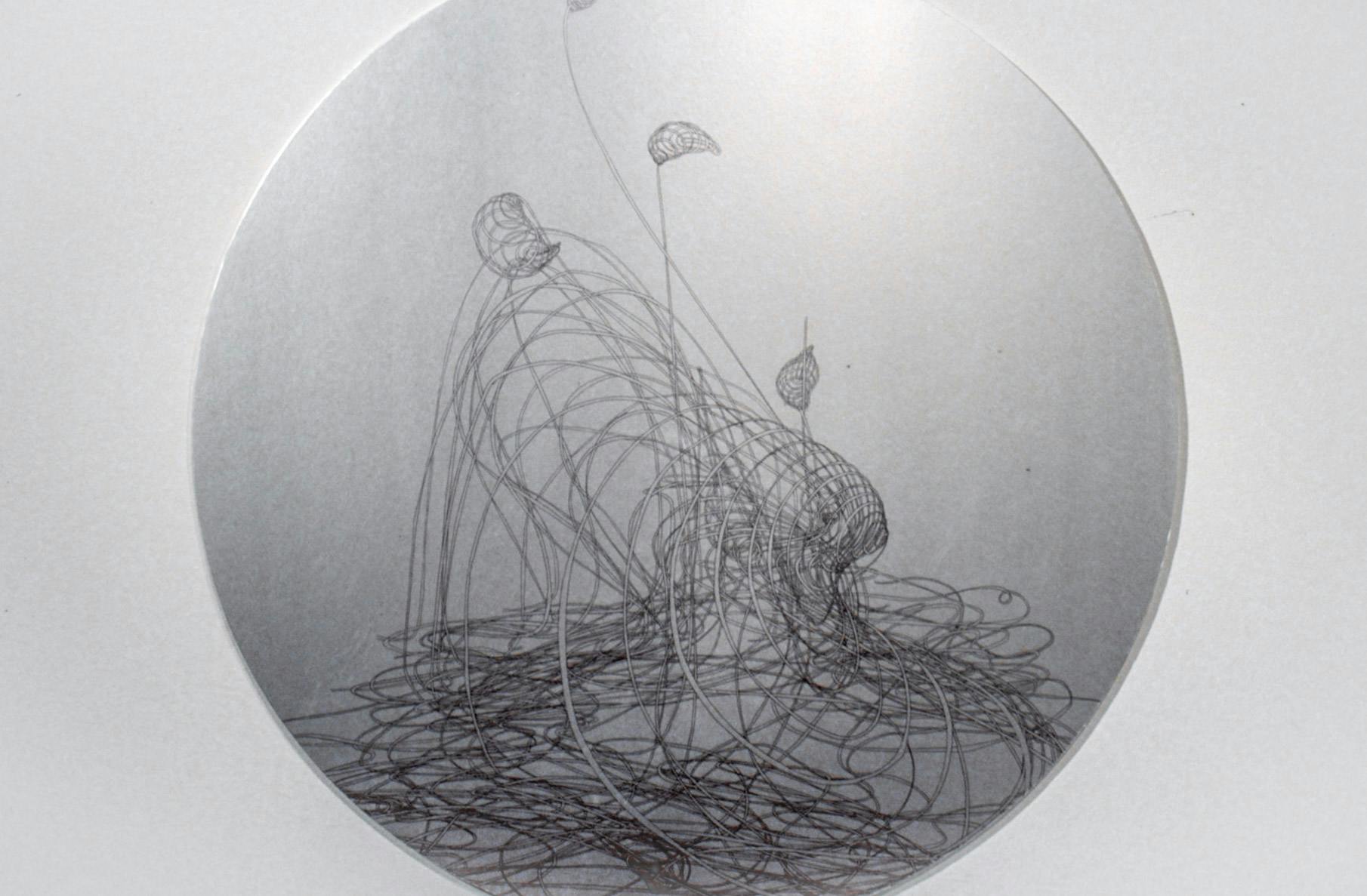 This is a close-up view of a circular shaped sculpture made by Lucy Pullen. On its silver metallic surface, an abstract line drawing is made. The drawing looks like leaves emerging from fishing nets.