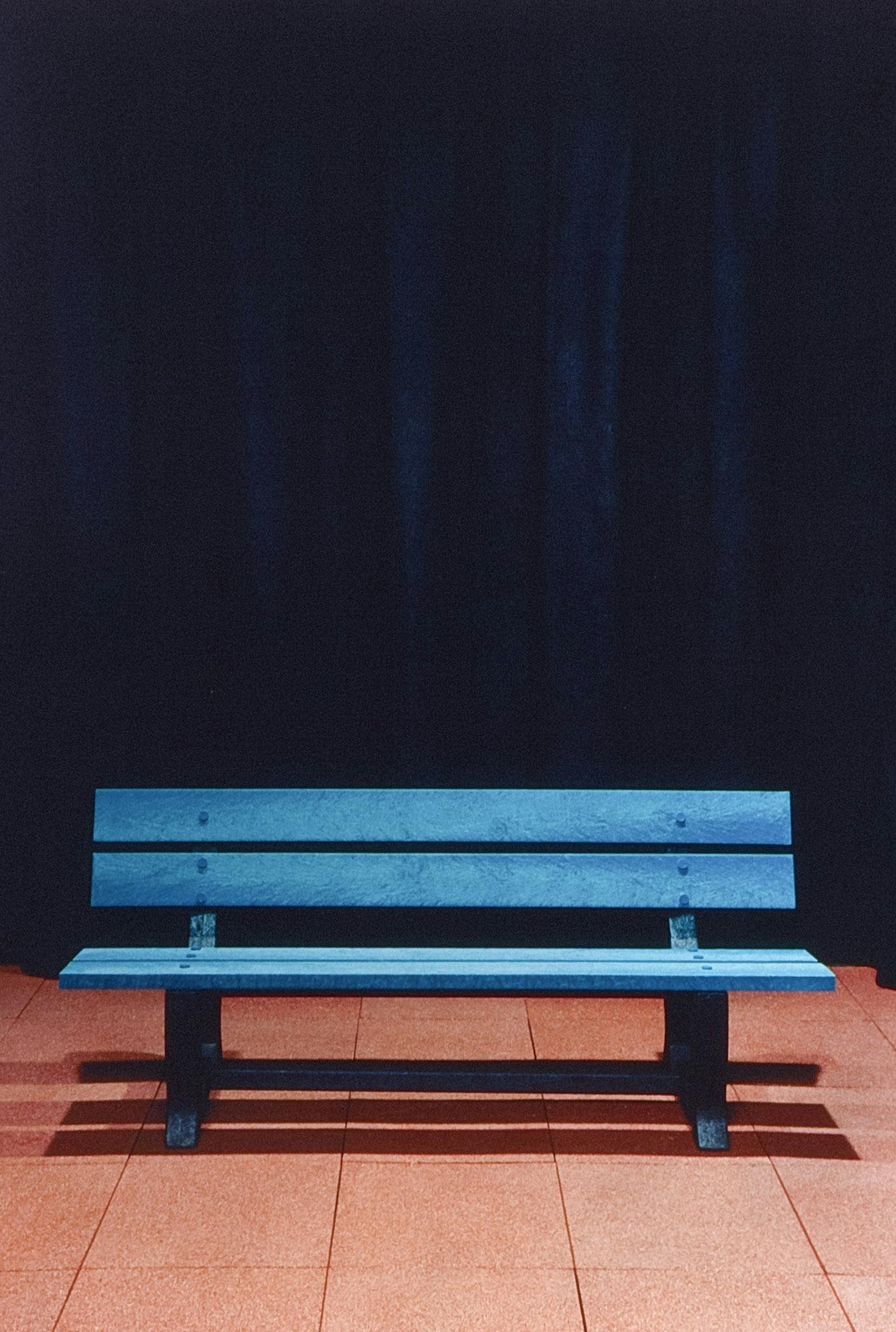 A blue wooden bench is installed in the gallery space. The background wall is covered by the navy blue curtain, and the gallery floor is covered by the oranger rubber tiles. 