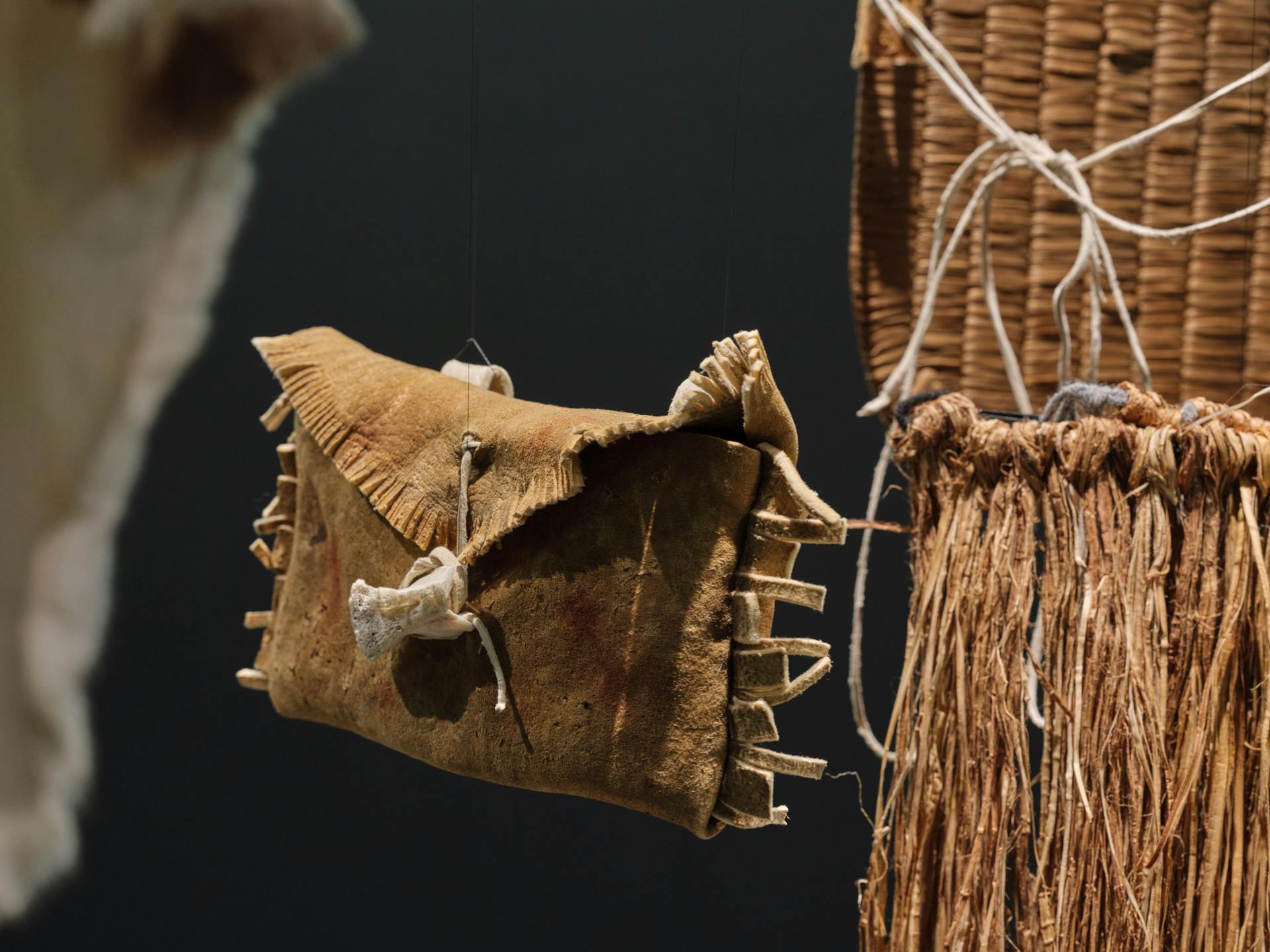 a suspended envelope-shaped bag made of tanned leather suspended between the edges of a hide robe and cedar war apron and breastplate. the bag is fringed on its right and left edges and on the edge of the flap, and held closed by a small bone.
