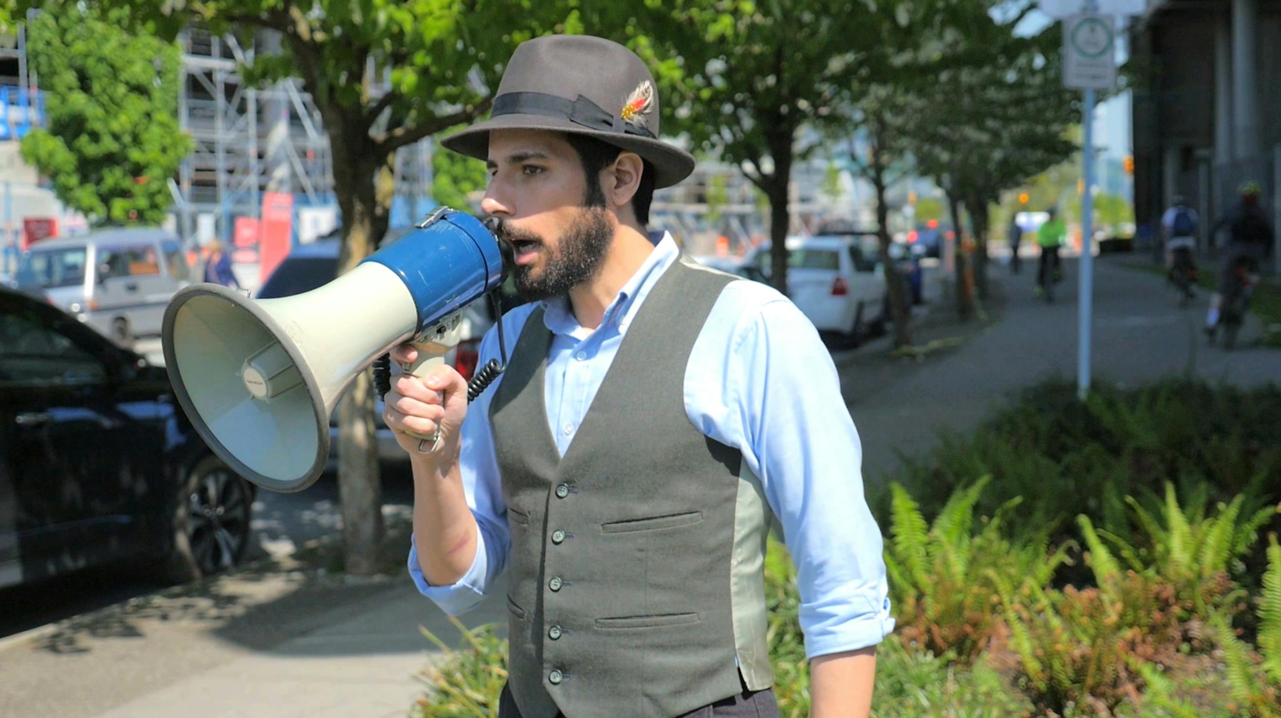 A photograph of Carmen Papalia speaking into a white megaphone on a street. 