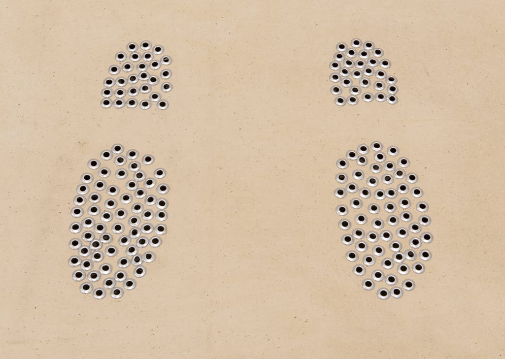 An artwork depicting two shoeprint-like forms made out of googly-eye stickers on a tan background. 