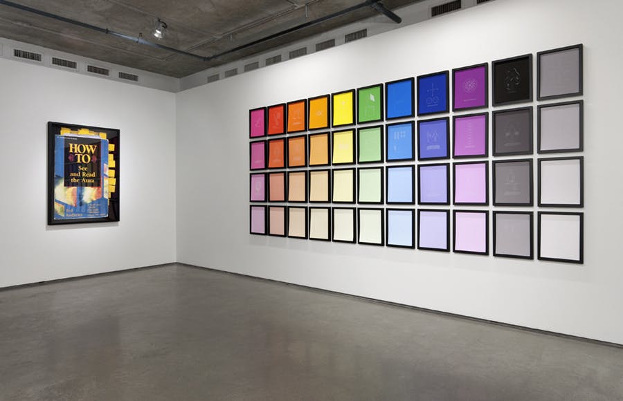 Forty-four framed artworks mounted on a wall in eleven columns. Each column is a different colour gradient. Mounted on an adjacent wall is a framed photograph of a blue cover.
