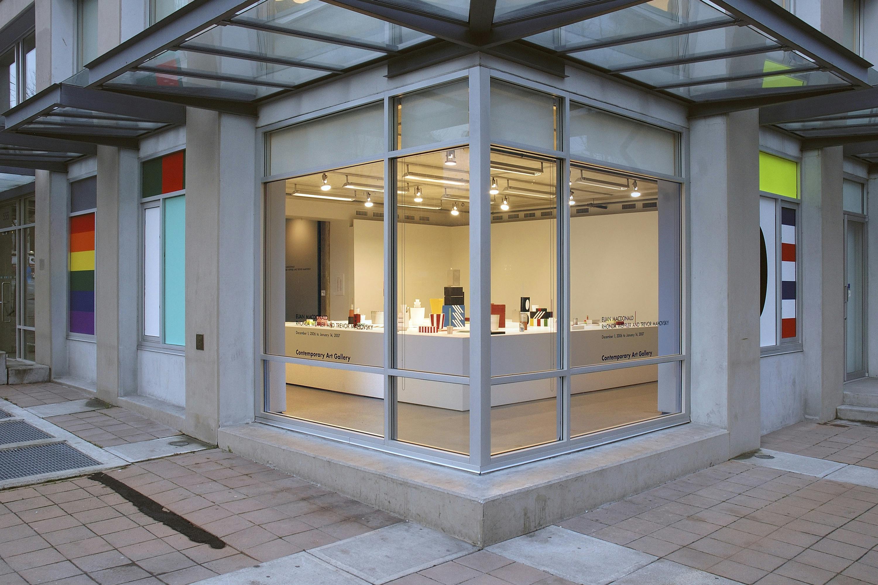 An image taken outside CAG looking into the inside gallery space through glass windows at the corner of Nelson and Richard Streets. Various sized sculptures are placed in a gallery on a large pedestal.