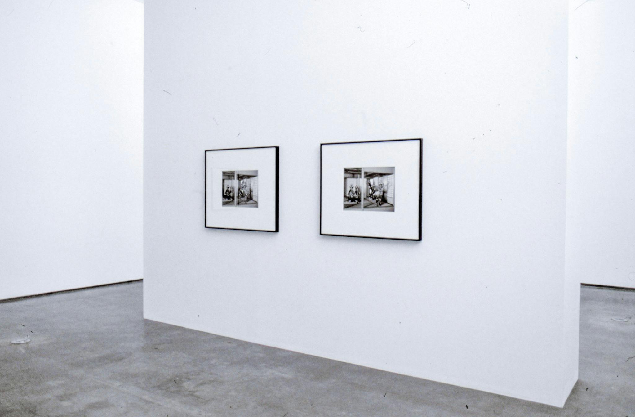 An install image of two black and white photographs on a gallery wall. Both photographs show a similar image of three people in a Japanese-style room, in which floors are covered with tatami mats.