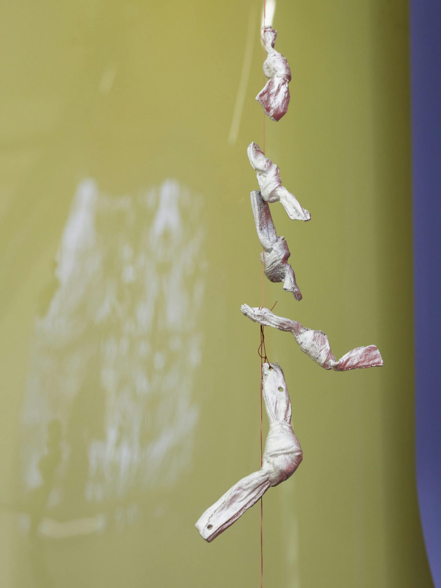 Silver sculptures hanging in a vertical arrangement from a string cast shadows on a hanging sheet of yellow photographic film.