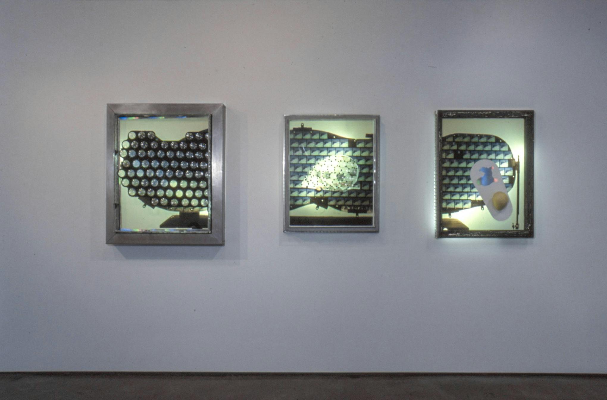 Installation image of Jerry Pethick’s artworks. On a wall, a set of three works that look like shadow muppets are installed in light box for exhibiting photography. Each of them are illuminated by pale-green light in the light boxes.