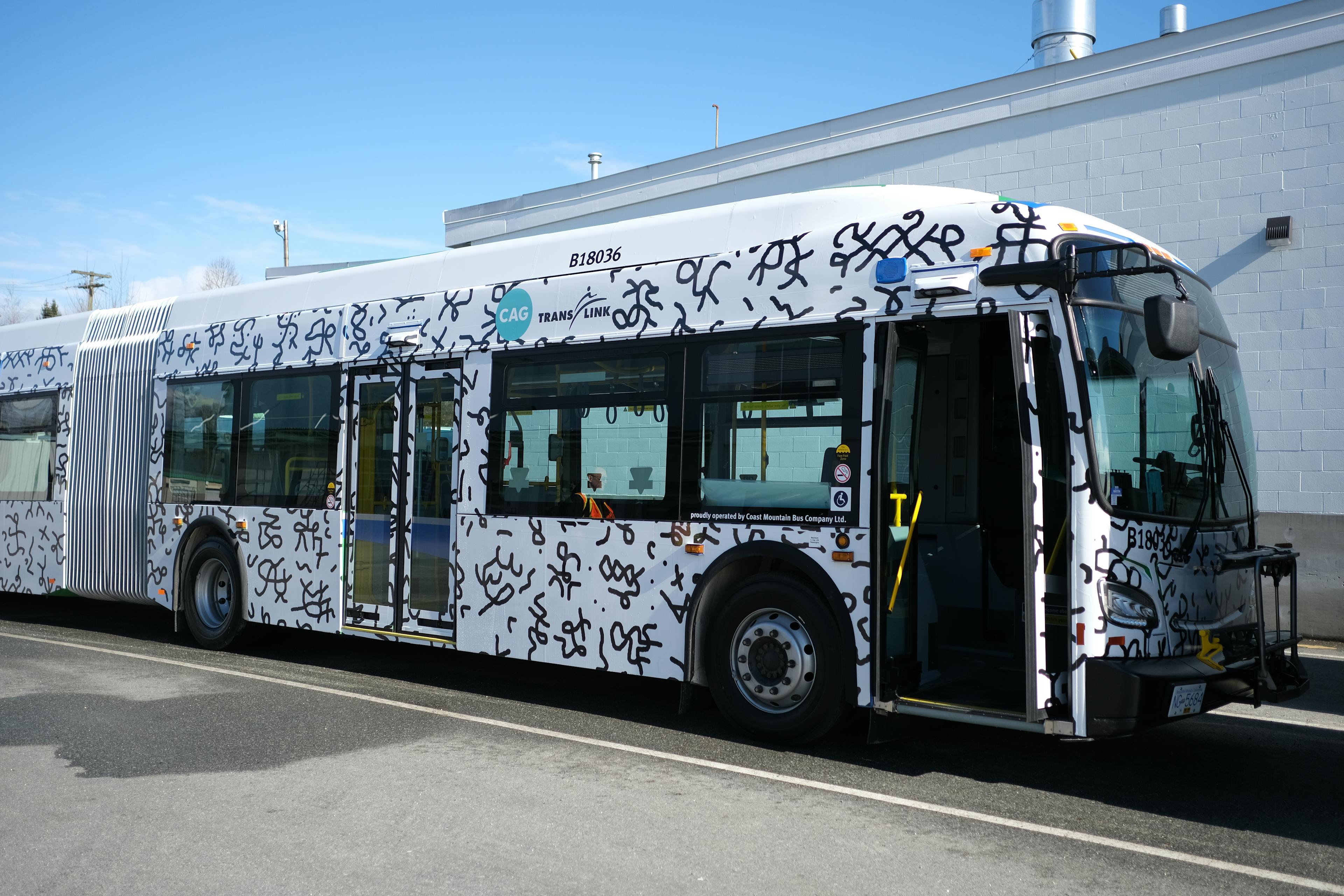 An image of the exterior of a transit bus that is wrapped in a patterned vinyl. The vinyl pattern is made up black pictographic imagery on a white background.   