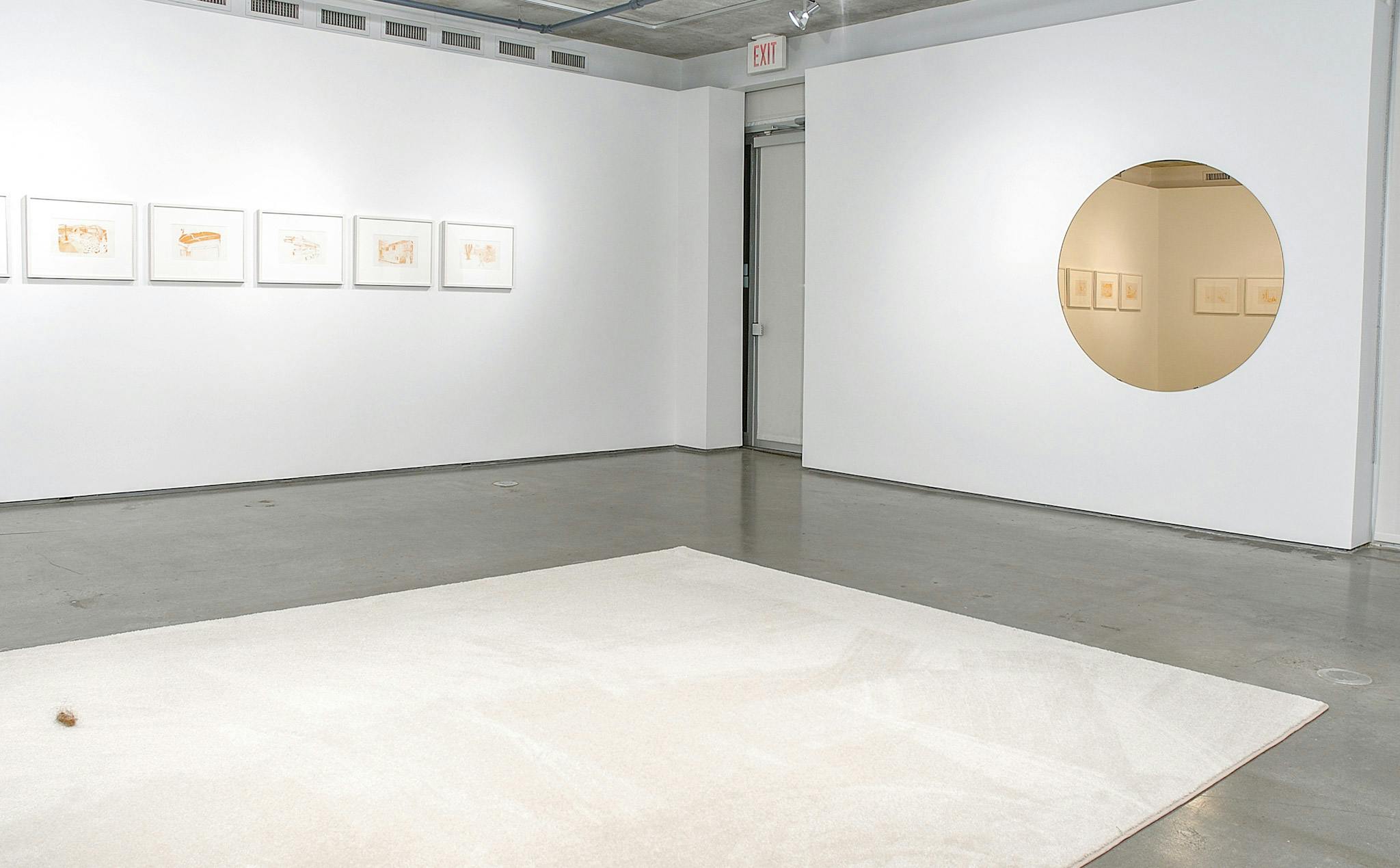 Orange drawings in white frames mounted on one wall of a gallery. On the perpendicular wall, a circular mirror reflects more of these drawings. There is a large white rug on the floor in the space.