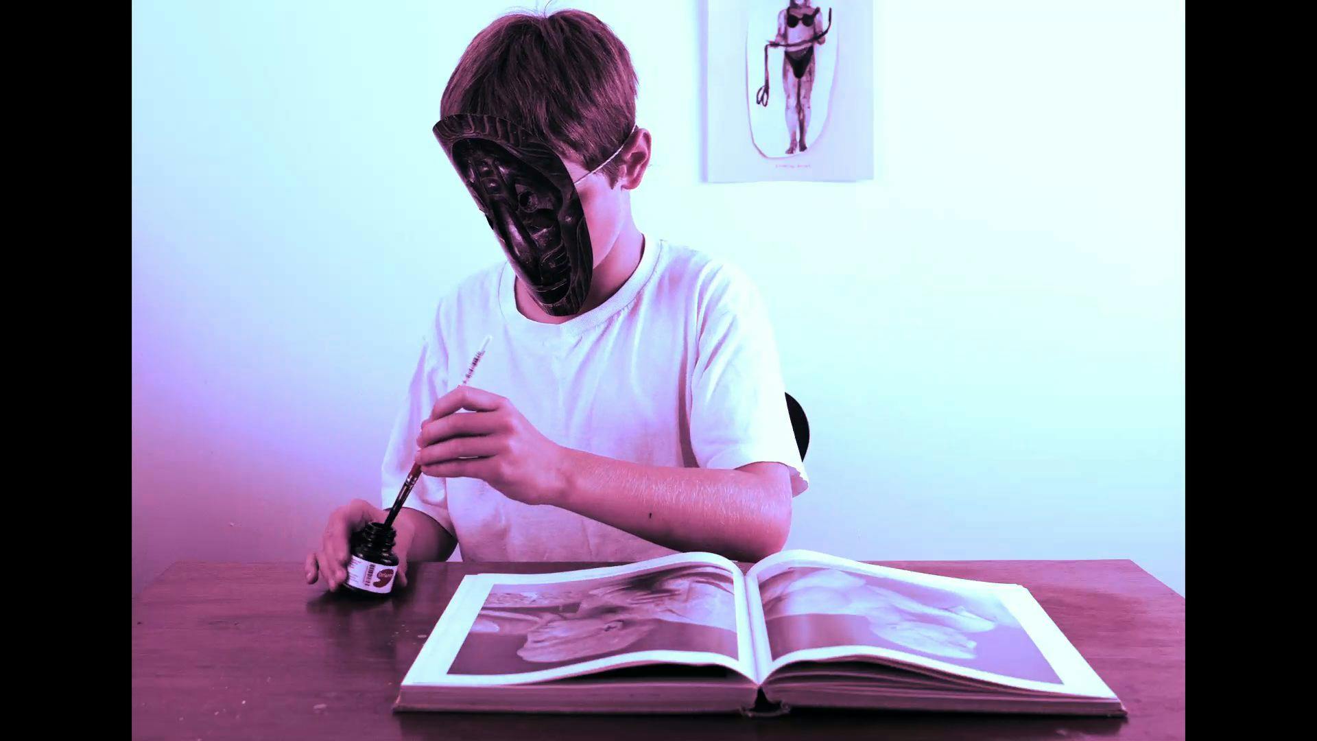 A child, wearing a mask and dipping a brush into an ink bottle, sits in front of an open book with photos of statues. A print hangs on the wall in the background. The entire image has a magenta hue.