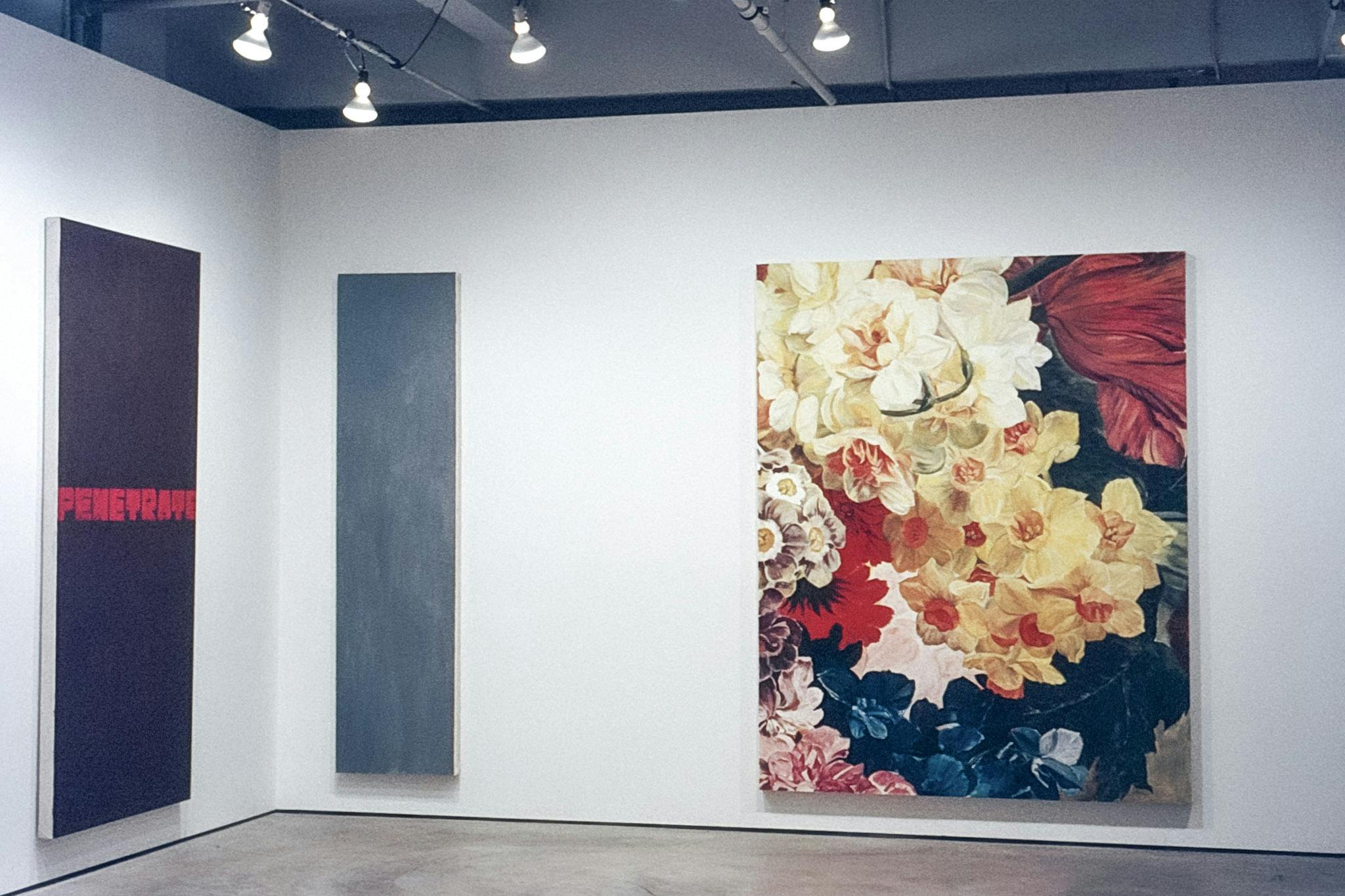 Three vertical paintings in a gallery. One painting has a dark background and the word "penetrate" written across in red, one painting is grey-blue and one shows various flowers, including daffodils.