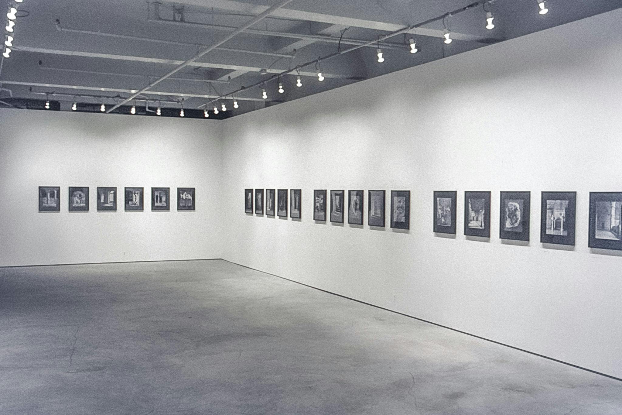 Several photos mounted across two walls of a gallery. The photos are black and white, mounted on black matte board in black frames, and show various architectural spaces, like stairways and arches.
