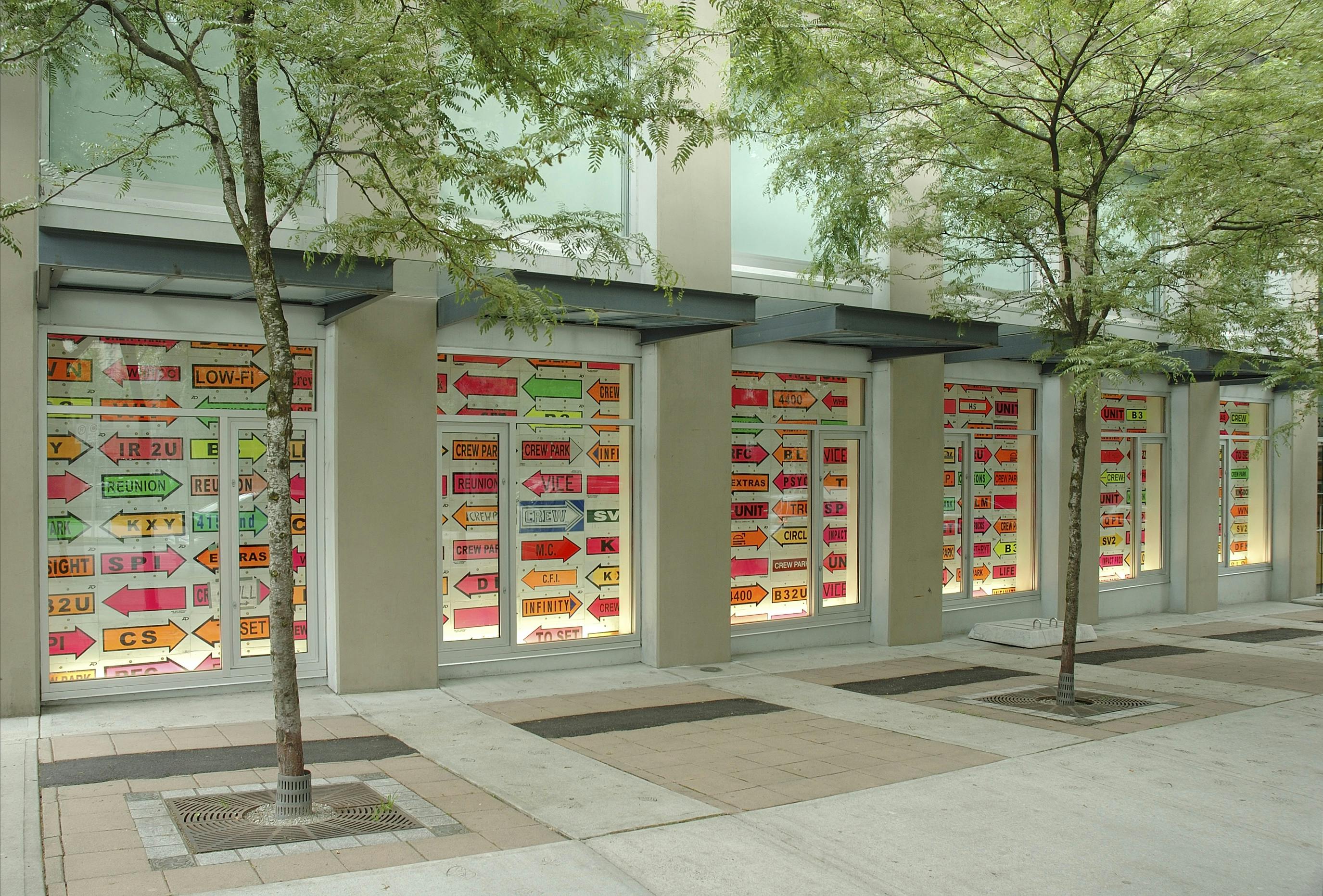 Neon-coloured signs cover the entire windows on the CAG’s facade. All the signs mimic the enlarged allow-shaped sticky notes with some words printed on them. Arrows point either to the left or right.