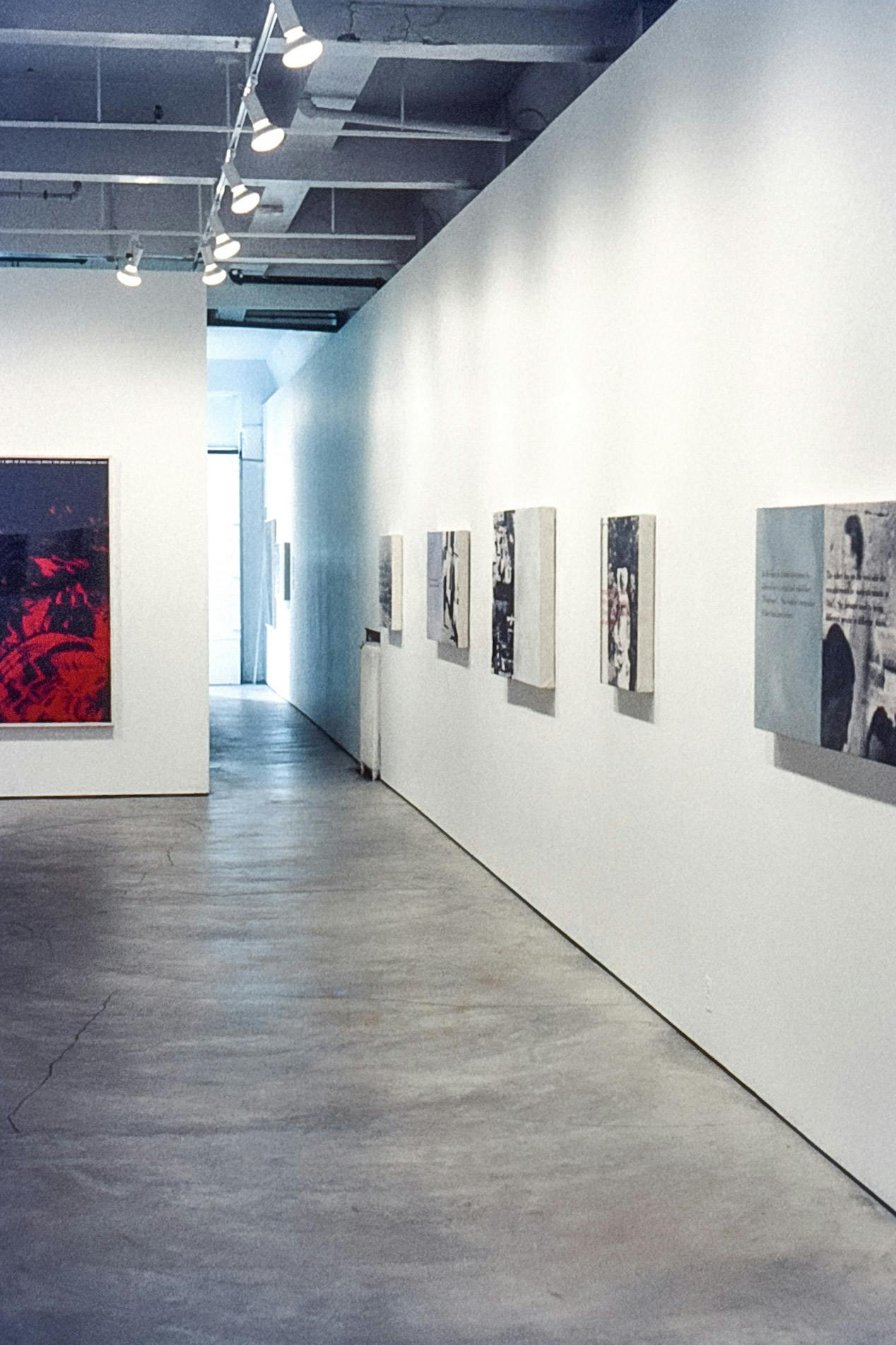 A photo of the installation view in the gallery. All of the five artworks mounted on the right-hand wall have black and white photographs accompanied by texts written beside or over the photographs.