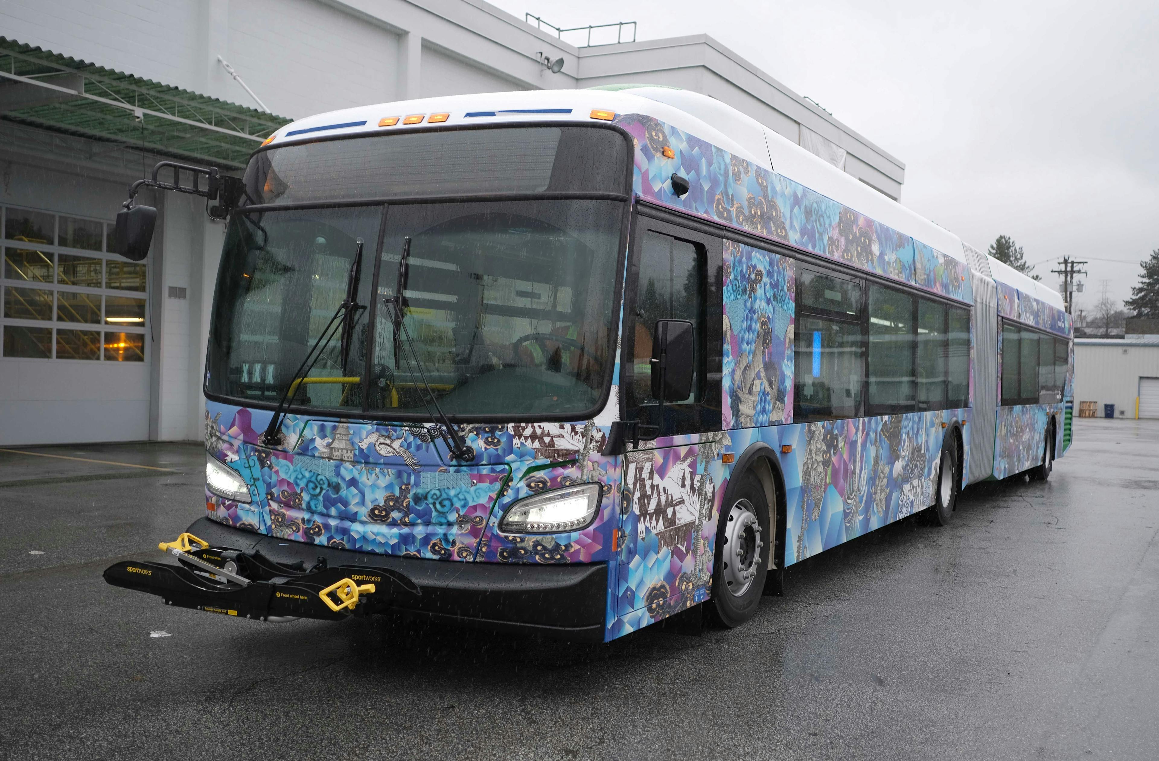 An image of the exterior of a transit bus that is wrapped in a patterned vinyl. The vinyl pattern is made up of a purple and blue geometric background with various illustrations superimposed on top.
