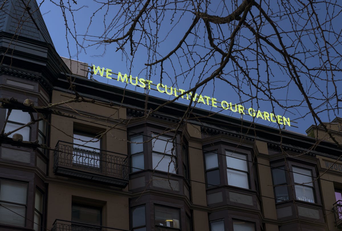 Nathan Coley’s work installed on the top loof of the Pennsylvania Hotel on East Hastings St. The Illuminated text reads “WE MUST CULTIVATE OUR GARDEN” in yellow-green light in the late evening sky.