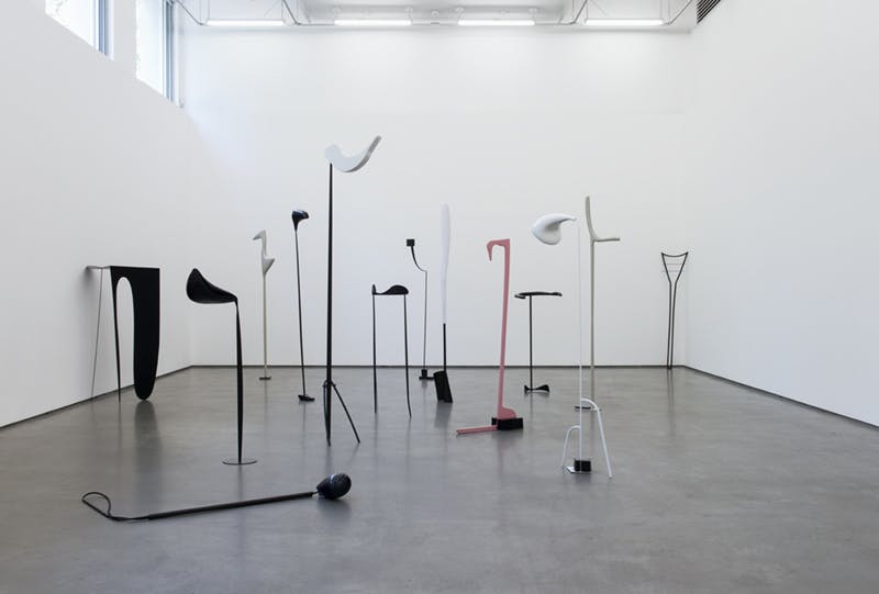 A series of tall, abstract sculptures by Nairy Baghramian installed in a gallery. Many of them, free-standing on the floor, appear to have long necks with thin heads. Their shapes resemble music notes.