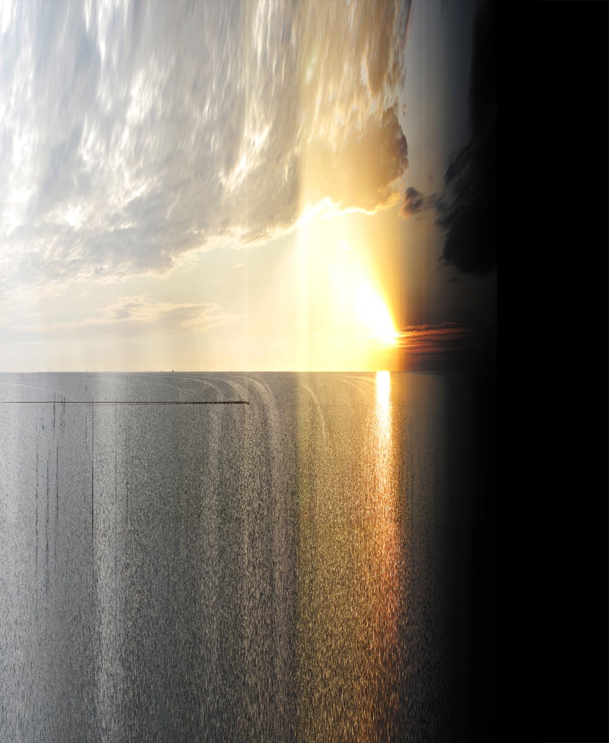 A photograph capturing the sun setting on the sea. A cloud covers the top left part of this image. One-third of this image on the right is covered by a black shadow.  