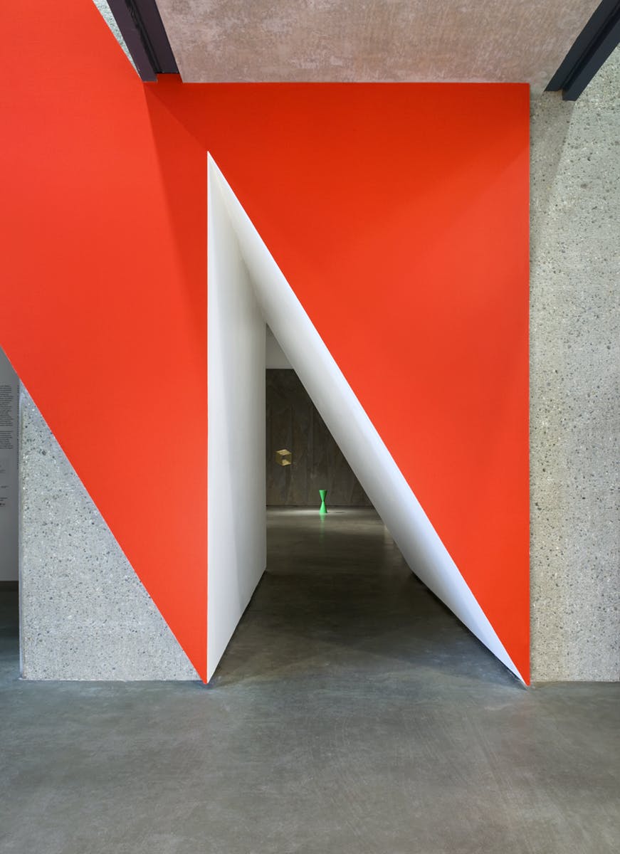 Robert Orchardson’s installation transforms an entryway to a gallery. A bold, red geometric facade with a triangular opening in the middle leads visitors through a white, angled tunnel to the gallery.