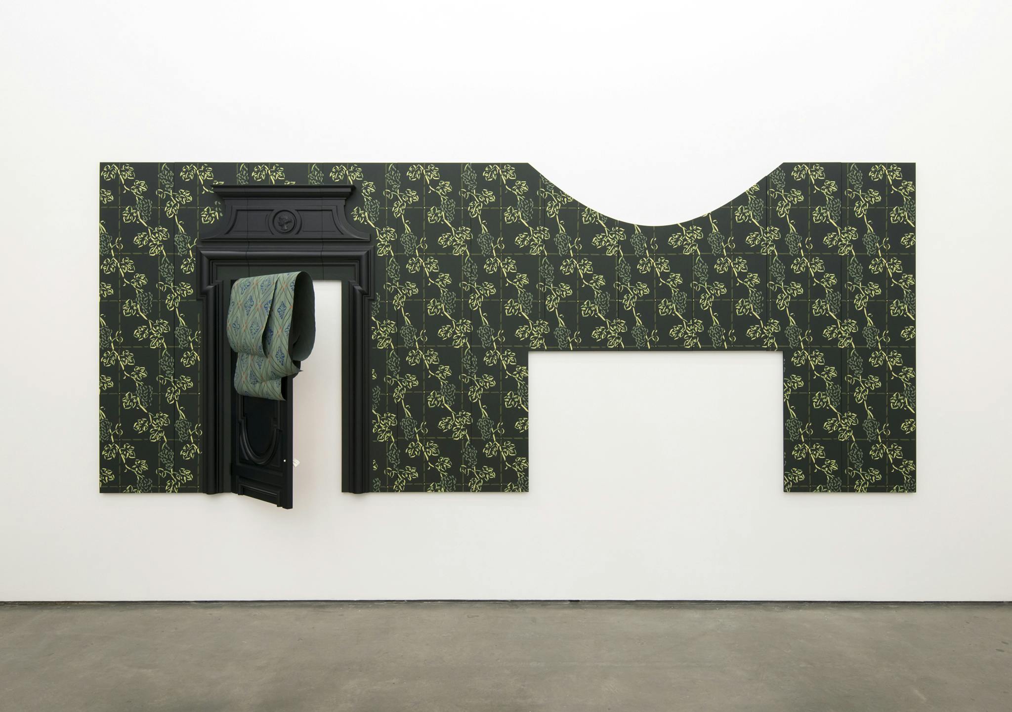 A rectangular section of floral wallpaper hangs on the gallery wall. A door within the wallpaper is half open. A rectangle and a semicircle piece is cut out of the top and bottom of the wallpaper.