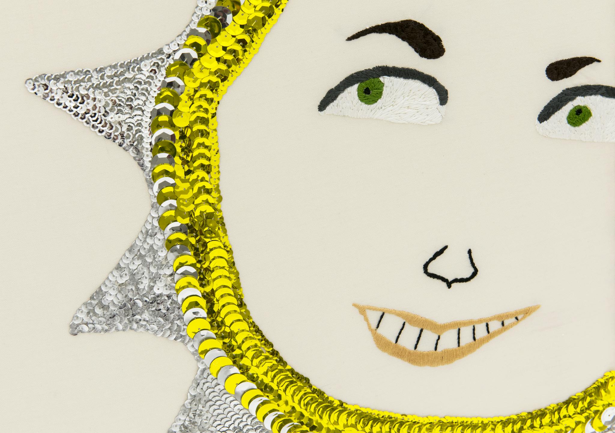 A detail of an embroidery sun with a grinning face.