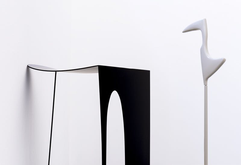 Detail image of Nairy Baghramian's sculptures. A black sculpture with two legs resembles a stool, while another in white, standing to the back, resembles the form of a resting heron.