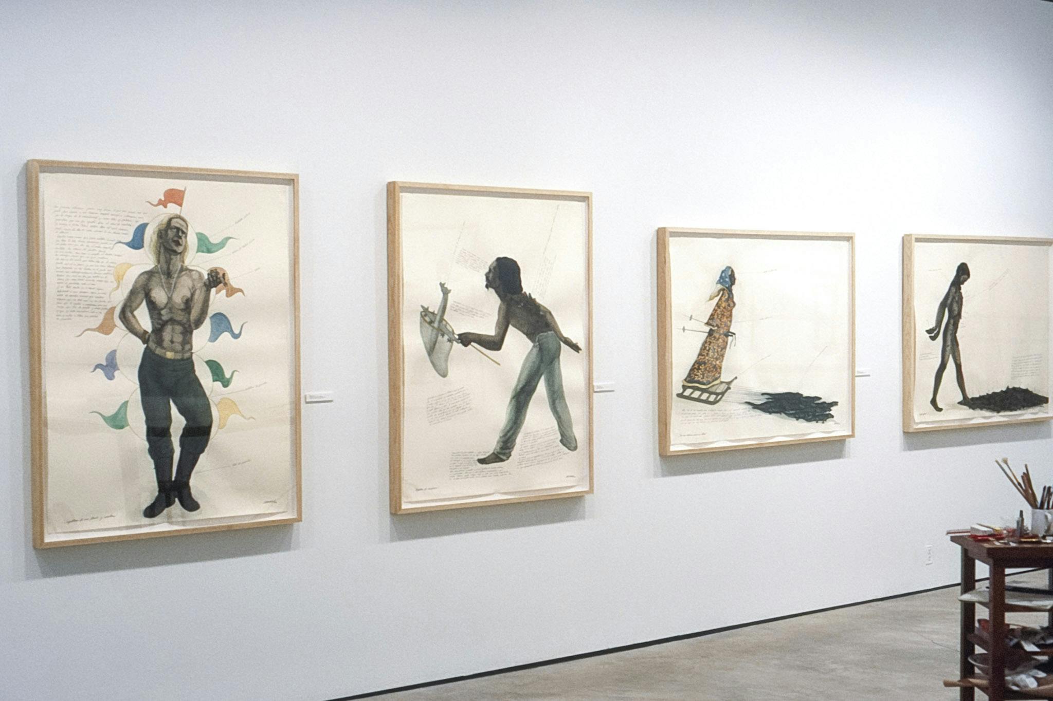 Four paintings of black-skinned people are installed on the gallery wall. The one on the far left shows a person with a gender-neutral body wearing small colorful flags. Some texts are written on each piece. 