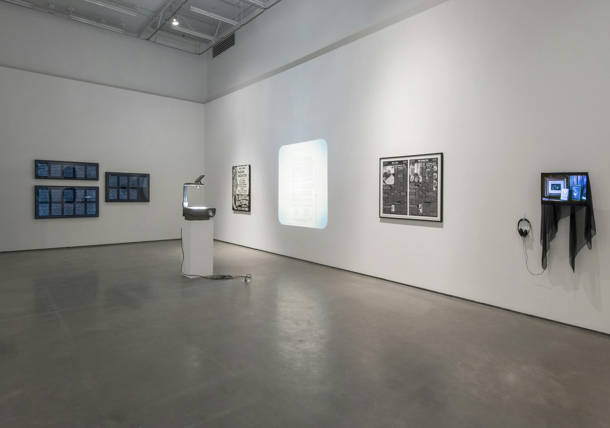 Multimedia works installed in a gallery: a video on a monitor, a framed print, an overhead projector projecting a text document, a black & white painting, and choreographic notes in three lightboxes.