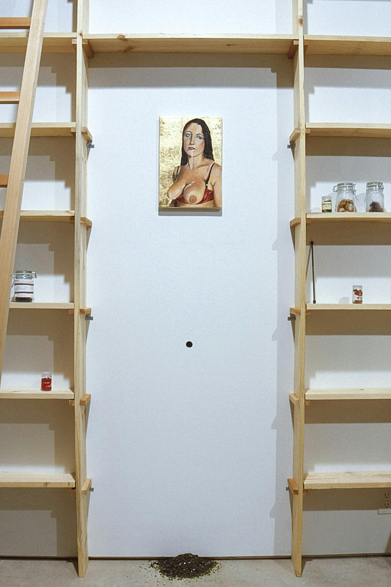 Tall wooden shelves, which one would expect to see in a pantry, are built in the gallery. On the wall behind the shelves, a topless woman’s painting is mounted above a small pile of dirt on the floor.