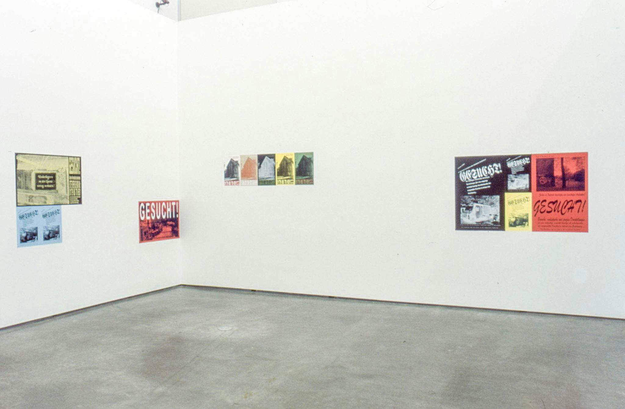 Installation image of posters by Alex Morrison. Five various-sized posters are mounted on the walls. The posters are coloured red, yellow, green, and light blue. Some of them are black and white.