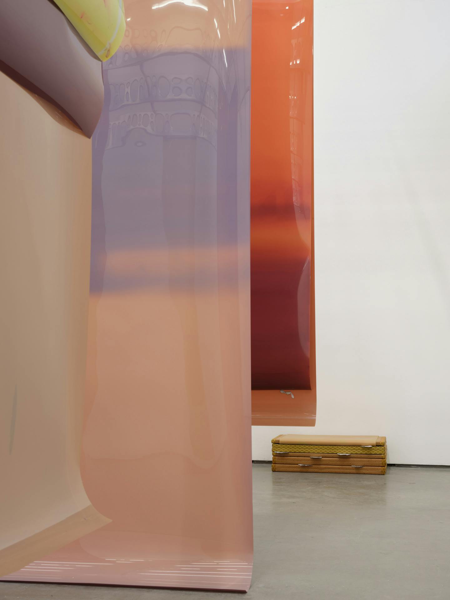Long earth tone sheets of film of various colours are suspended from the ceiling. A sculpture, made of tatami mats and cast aluminium objects, sits against a white wall in the background.⁠