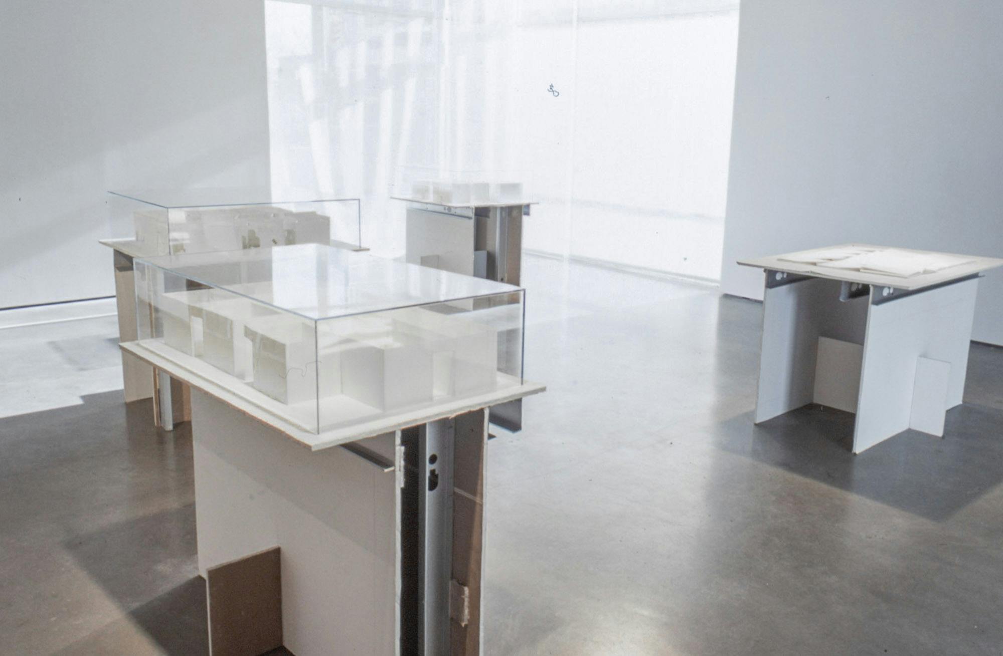 A set of white sculptures in display boxes are placed in a gallery space. Each sculpture displays a mockup of an architecture complex. 