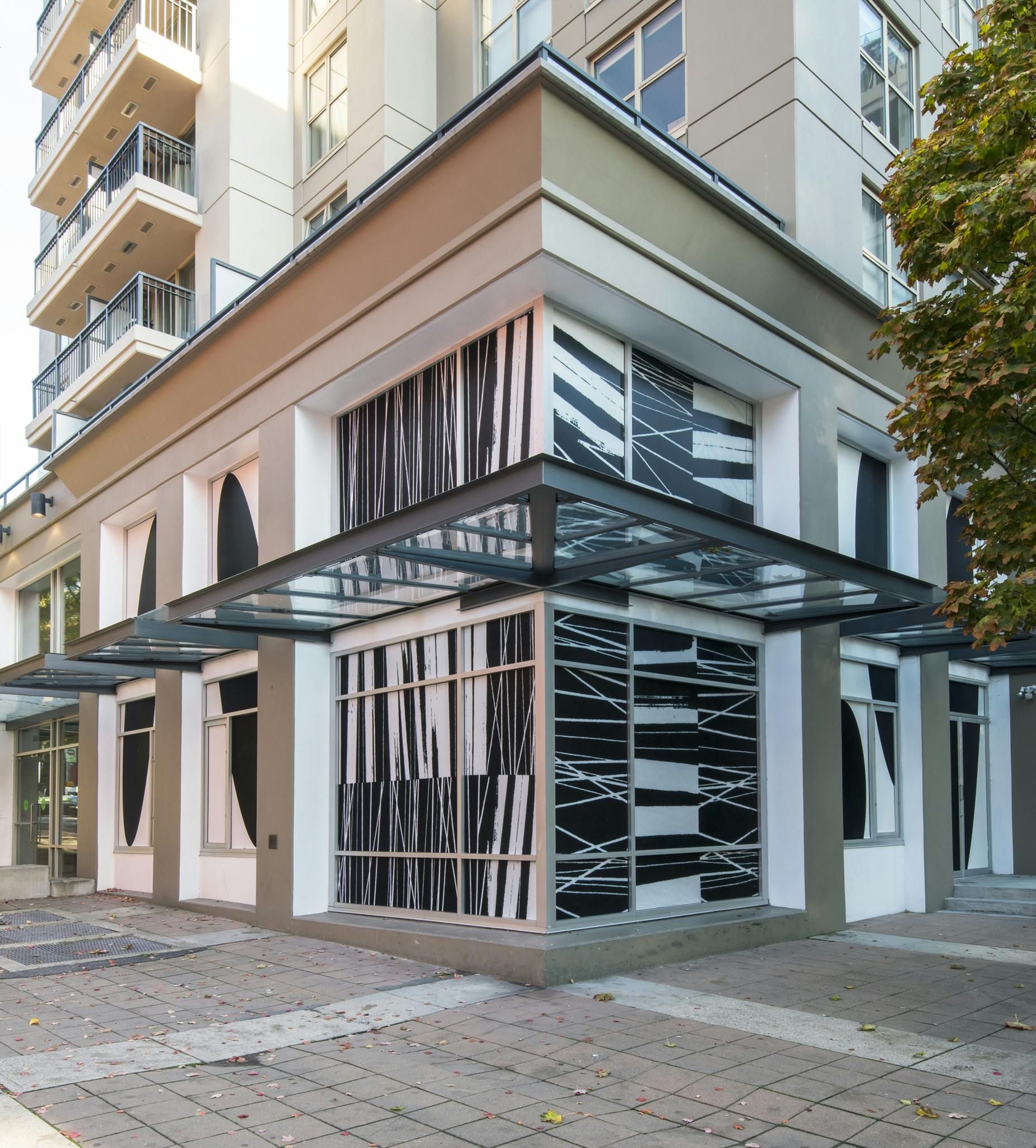 Exterior image of CAG with the work of Lyse Lemieux installed in vinyl across the ground and top floor windows. Large-scale black ellipses alternate with black linear patterns on a beige background.