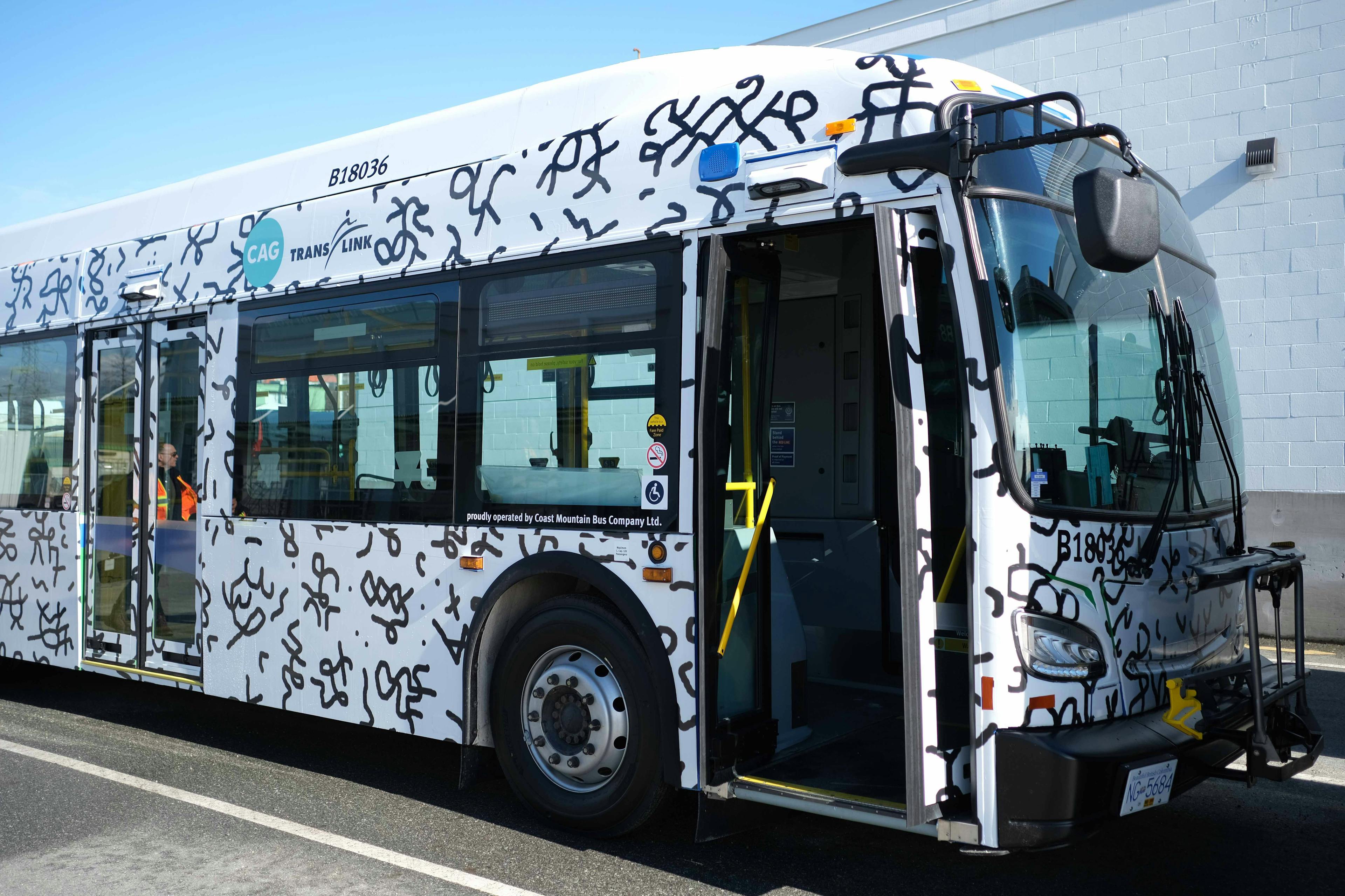 An image of the exterior of a transit bus that is wrapped in a patterned vinyl. The vinyl pattern is made up black pictographic imagery on a white background. 