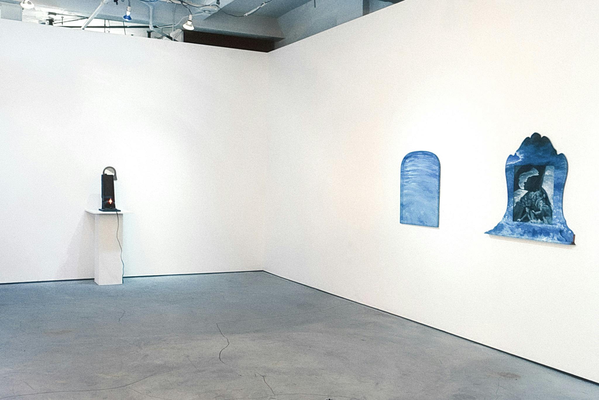 Three artworks in the corner of a gallery space. On one wall there are two small framed works that are painted as cloudy skies. On the other wall there is a small lightbulb in a box on a plinth. 