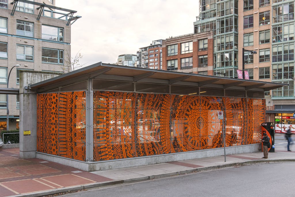 Exterior image of Yaletown-Roundhouse Station, with the station windows installed with Gunilla Klingberg’s work. A dark orange mandala-like pattern of cut vinyl covers the windows.