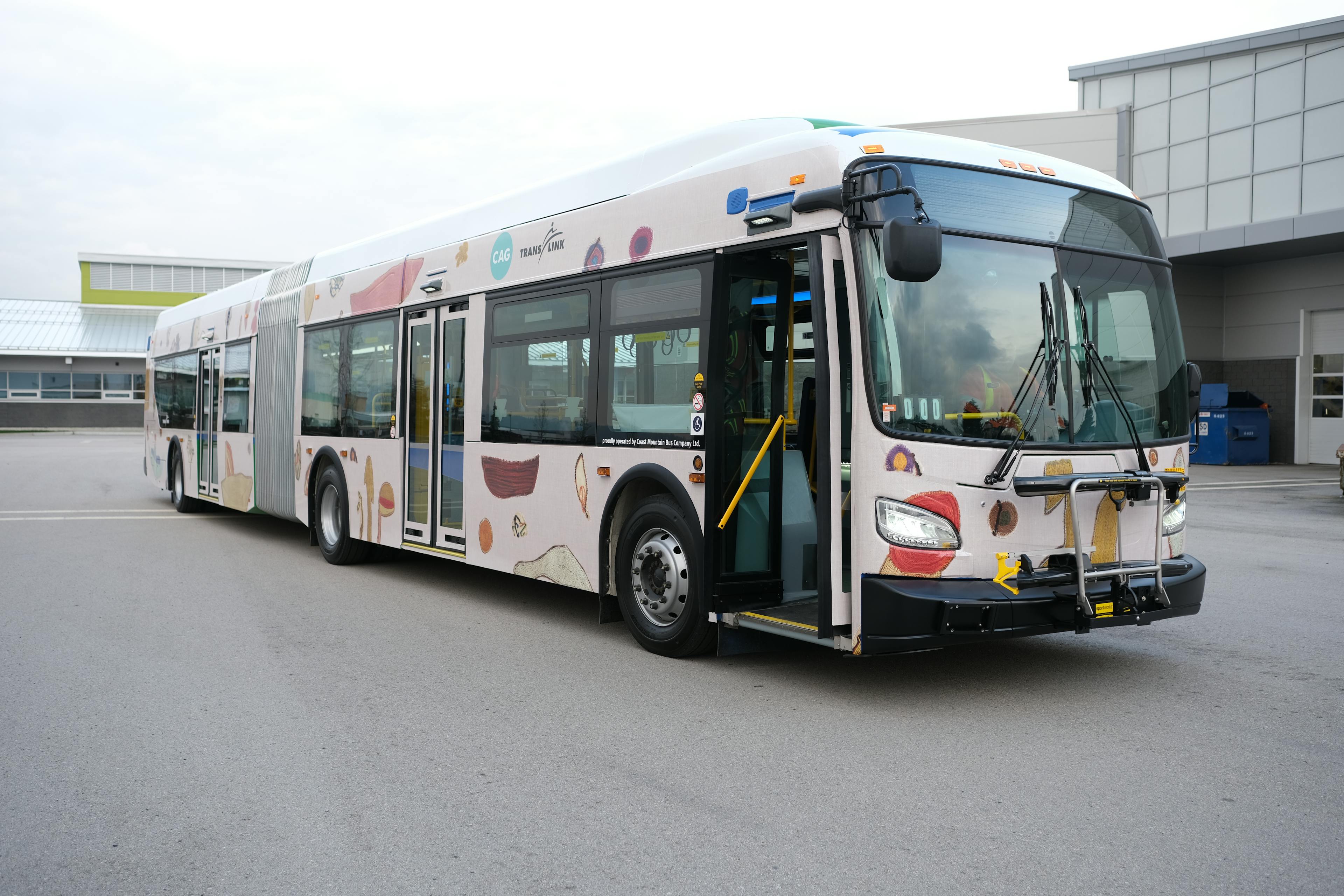 An image of the exterior of a transit bus that is wrapped in a patterned vinyl. The vinyl pattern is made up of a plain pink background with abstract illustrations of various forms and shapes. 