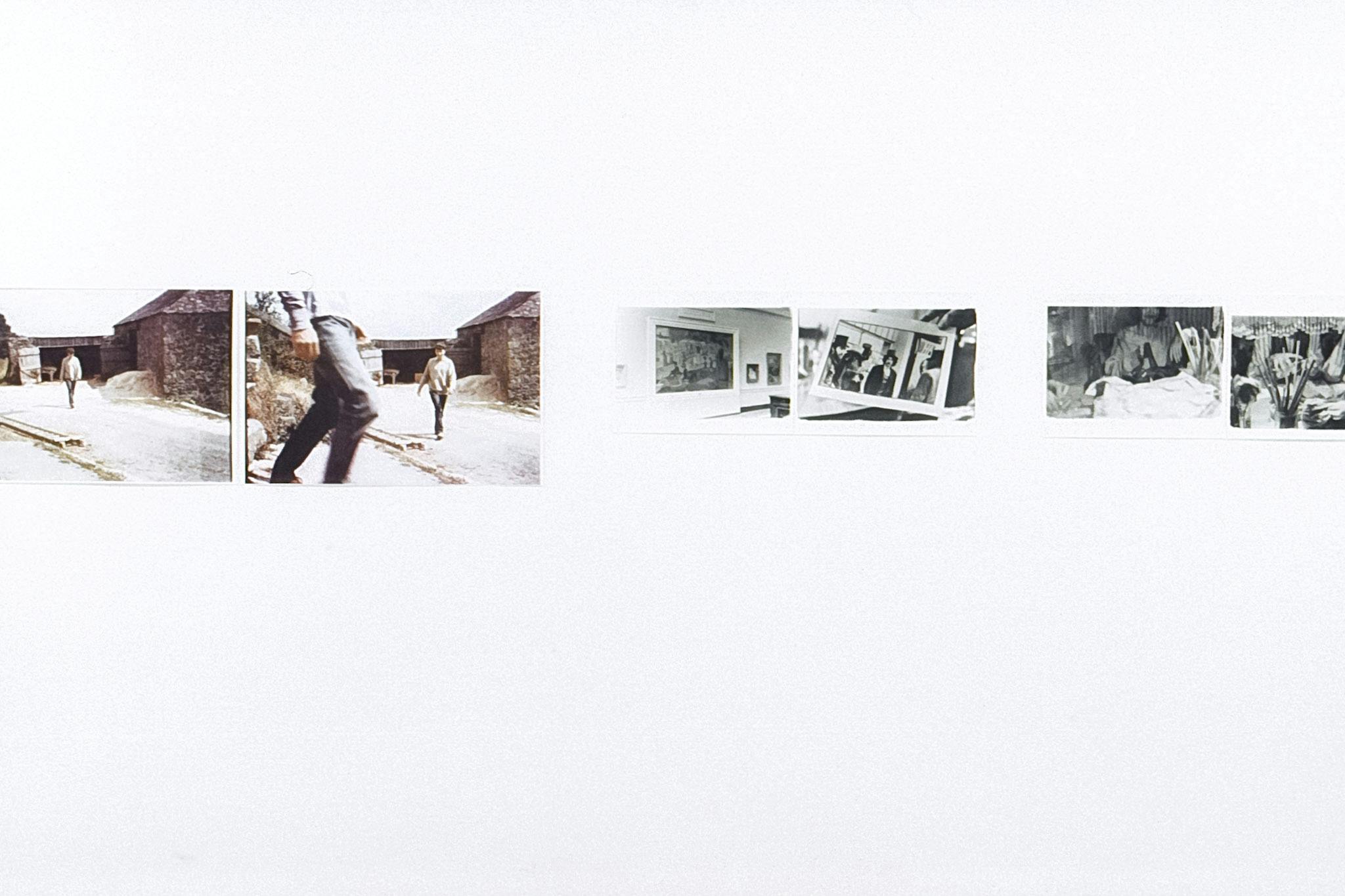 A closeup of six photos on a white wall. Two of the images are larger and in colour, showing people walking by a stone building. The other four are black and white, showing parties and photo books. 
