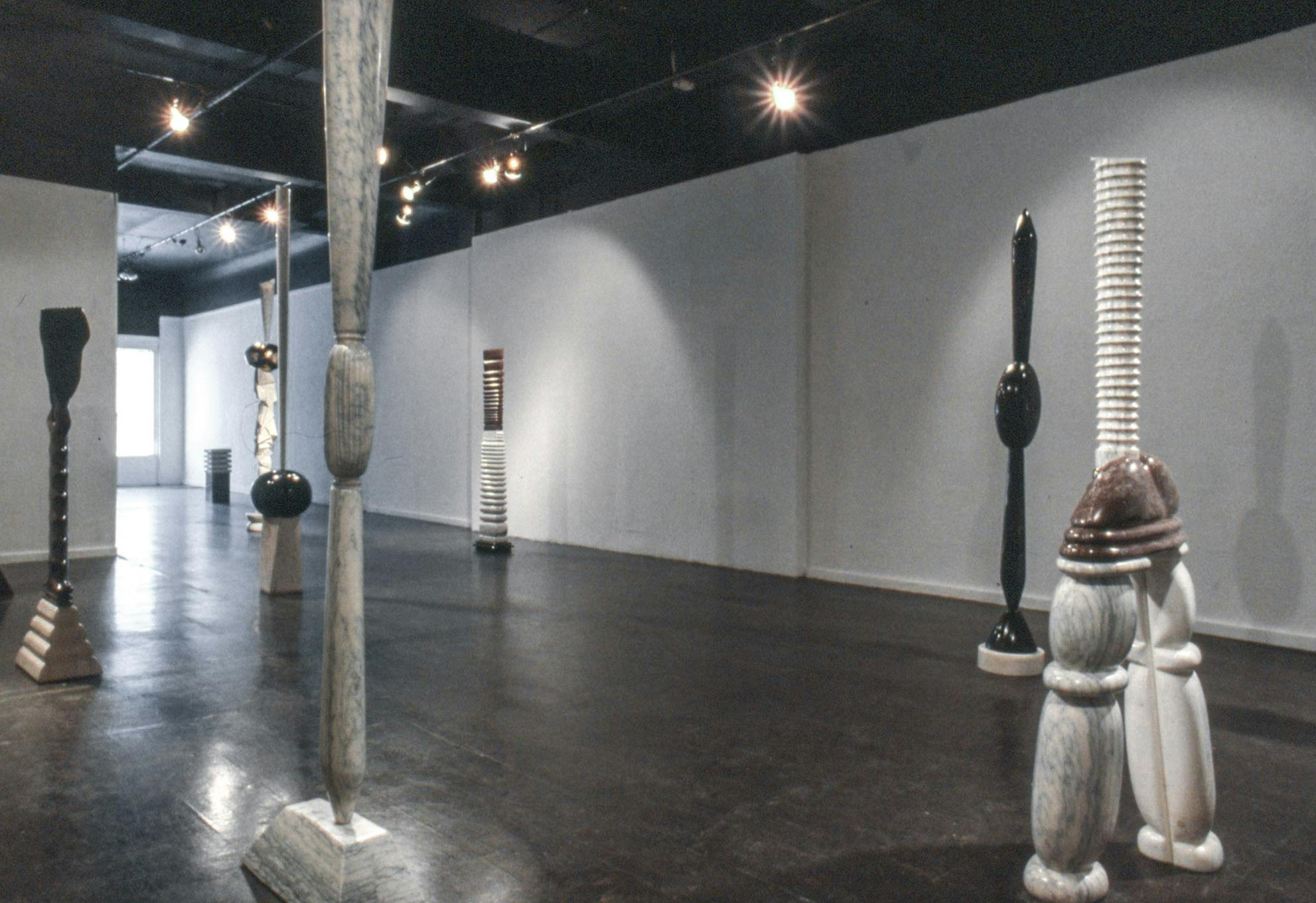 Several sculptures in a gallery space. The sculptures are made of different black, white, and brown stones. They are carved and stacked into different tall, ridged and bulbous forms.