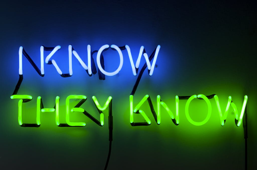 Phrases in blue and green neon lights read: “I KNOW THEY KNOW.” 